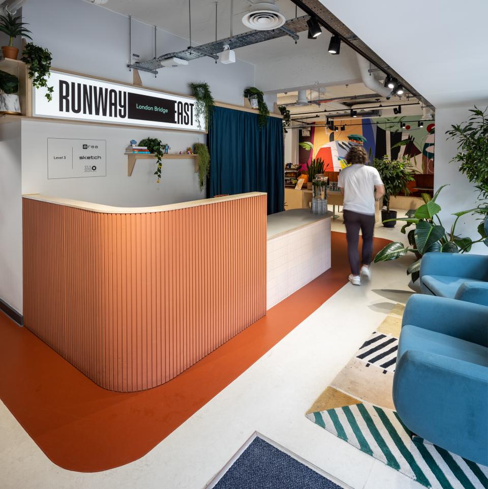 Runway East's vibrant reception area features colorful patterns, greenery, and modern design elements, promoting a collaborative workspace atmosphere.