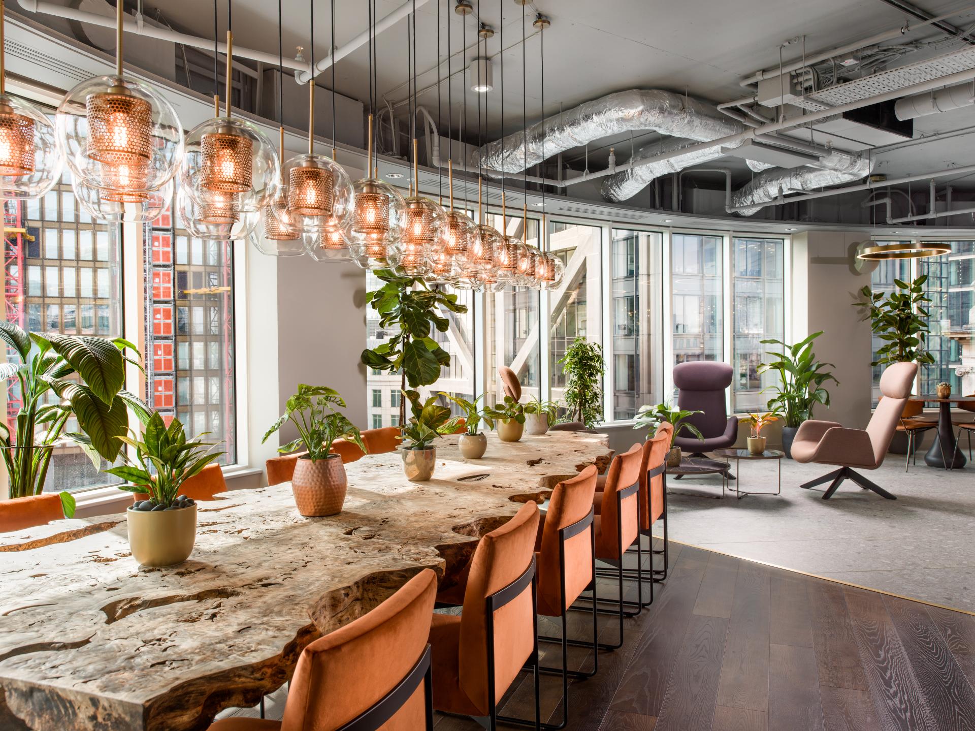 Modern workspace featuring a large wooden table, stylish seating, and vibrant plants for flexible working design.