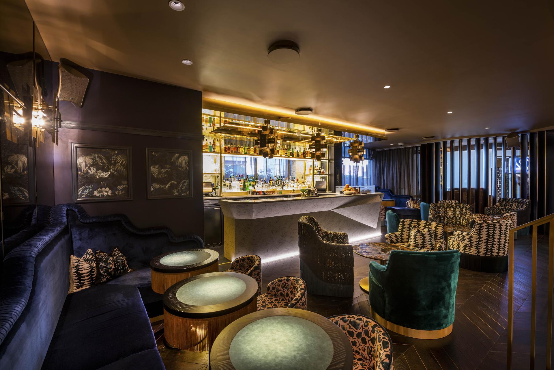 Elegant bar area of The Colony Club featuring luxurious seating, illuminated shelves, and a stylish ambiance reflecting Hollywood glamour.