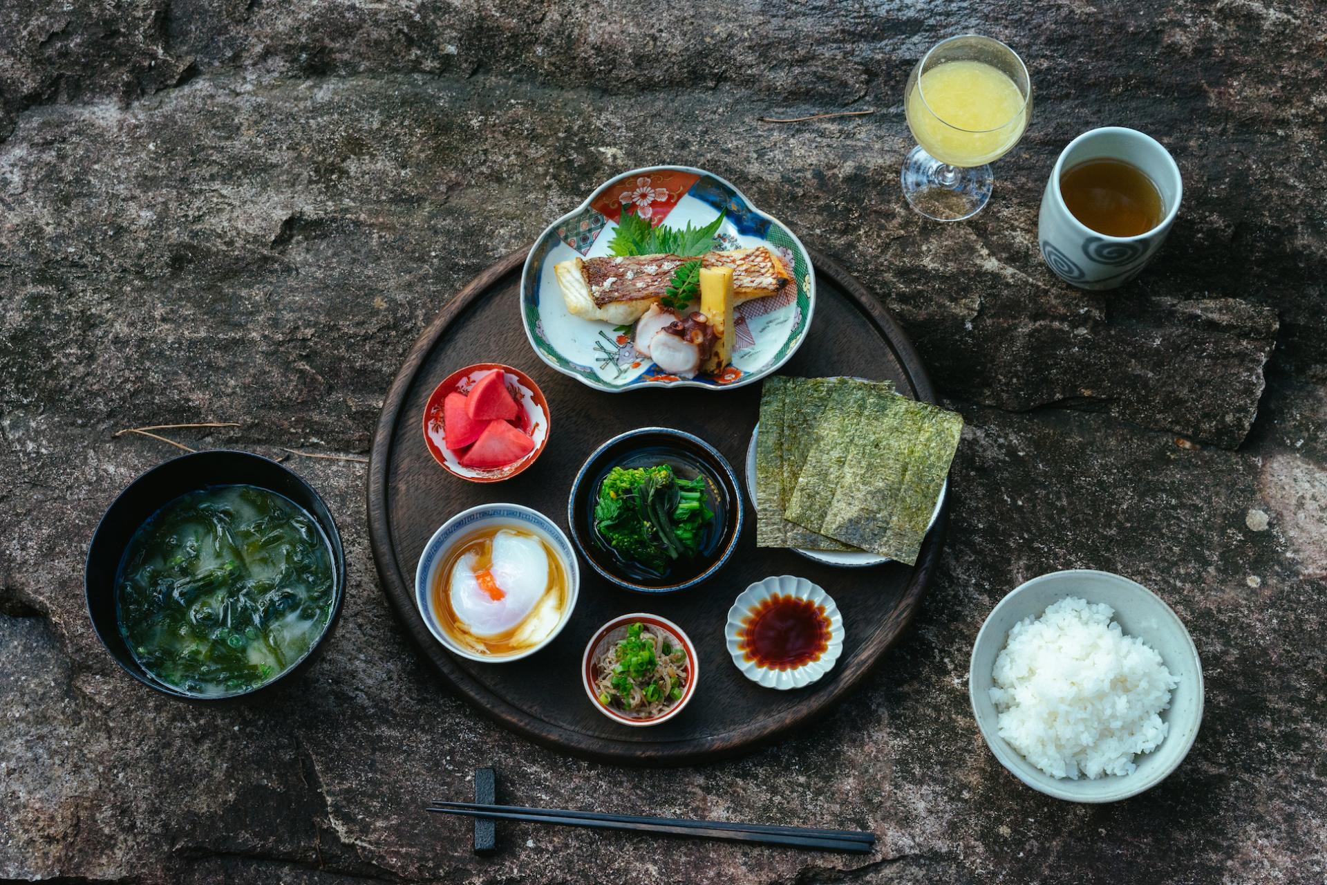 Traditional Japanese breakfast served on a wooden tray, featuring grilled fish, rice, miso soup, and fresh vegetables.
