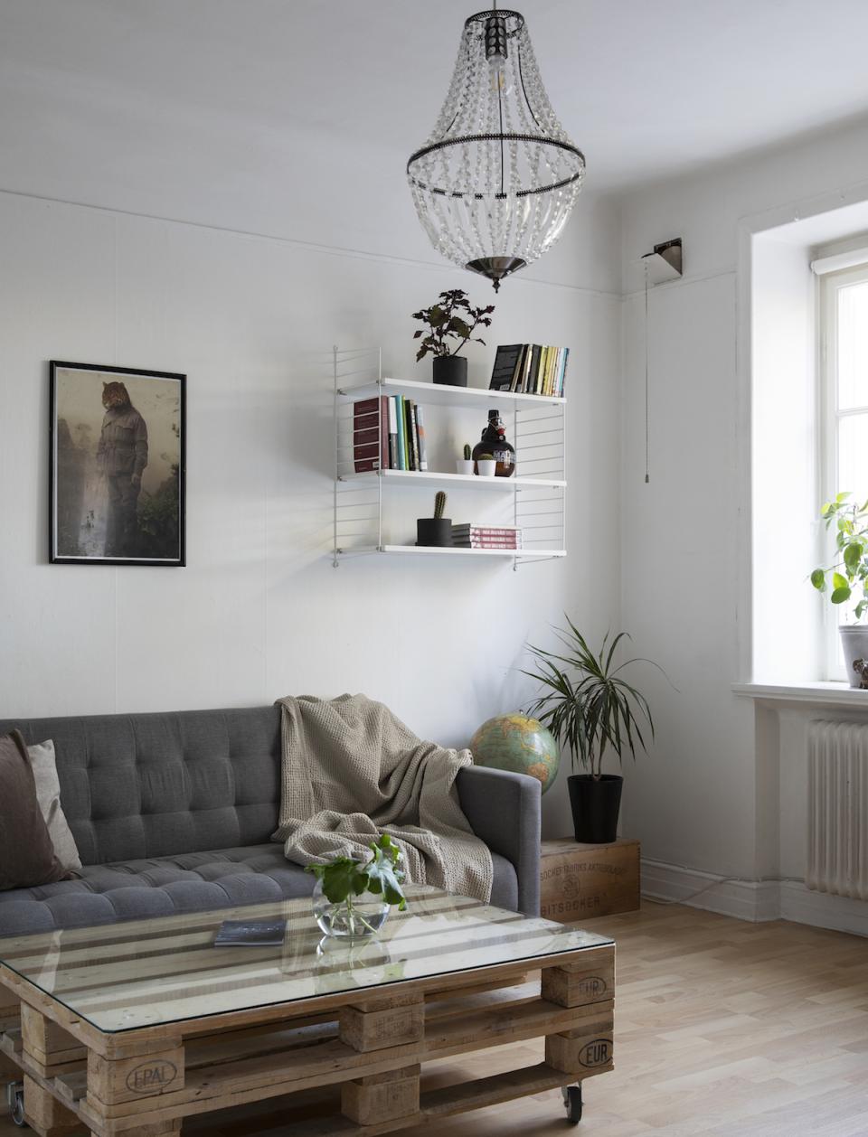 Cozy Scandinavian living room featuring a modern sofa, glass coffee table, bookshelves, and elegant chandelier.