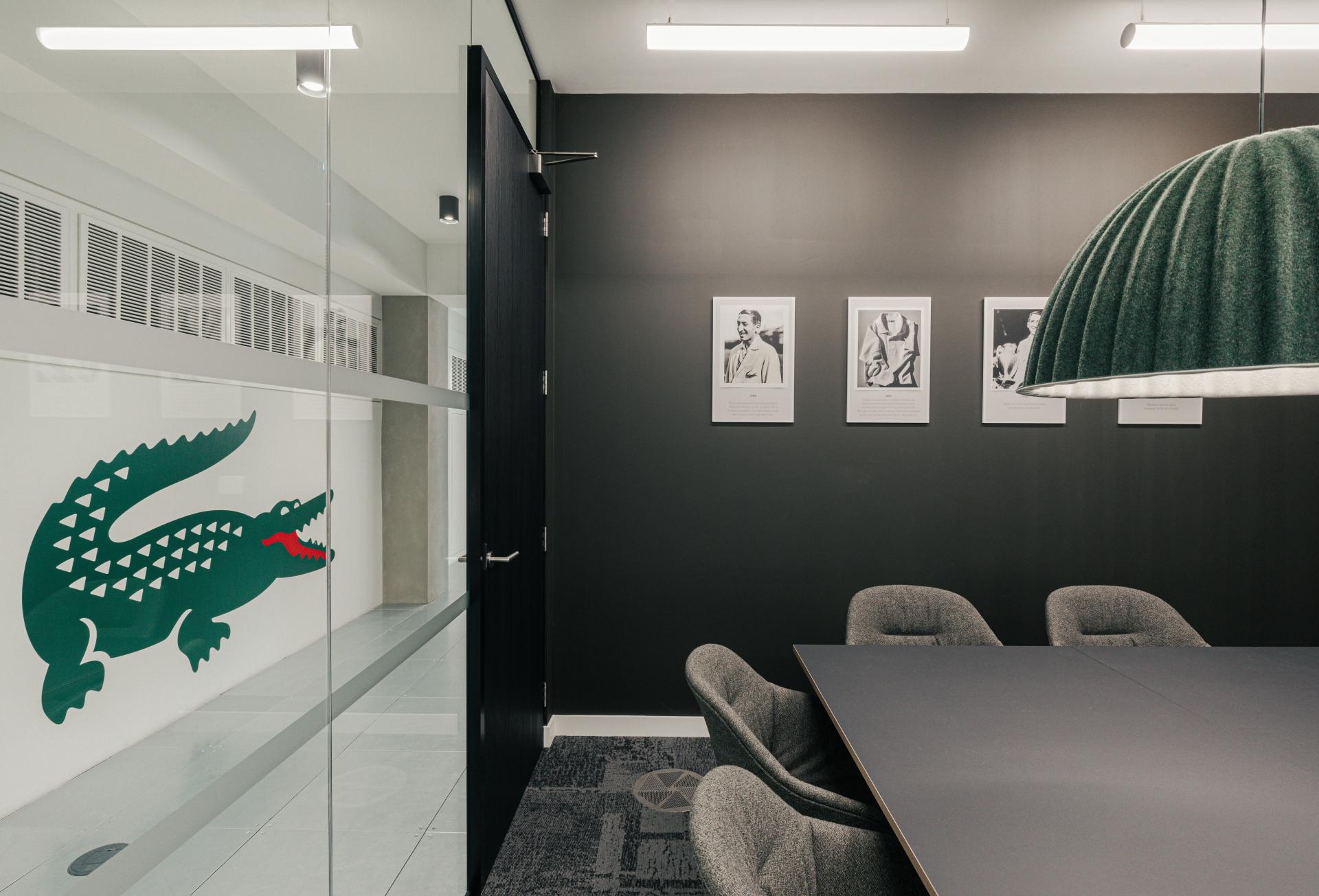 Modern conference room featuring Lacoste logo, stylish furniture, and art, reflecting New York warehouse aesthetic for Lacoste workspace.