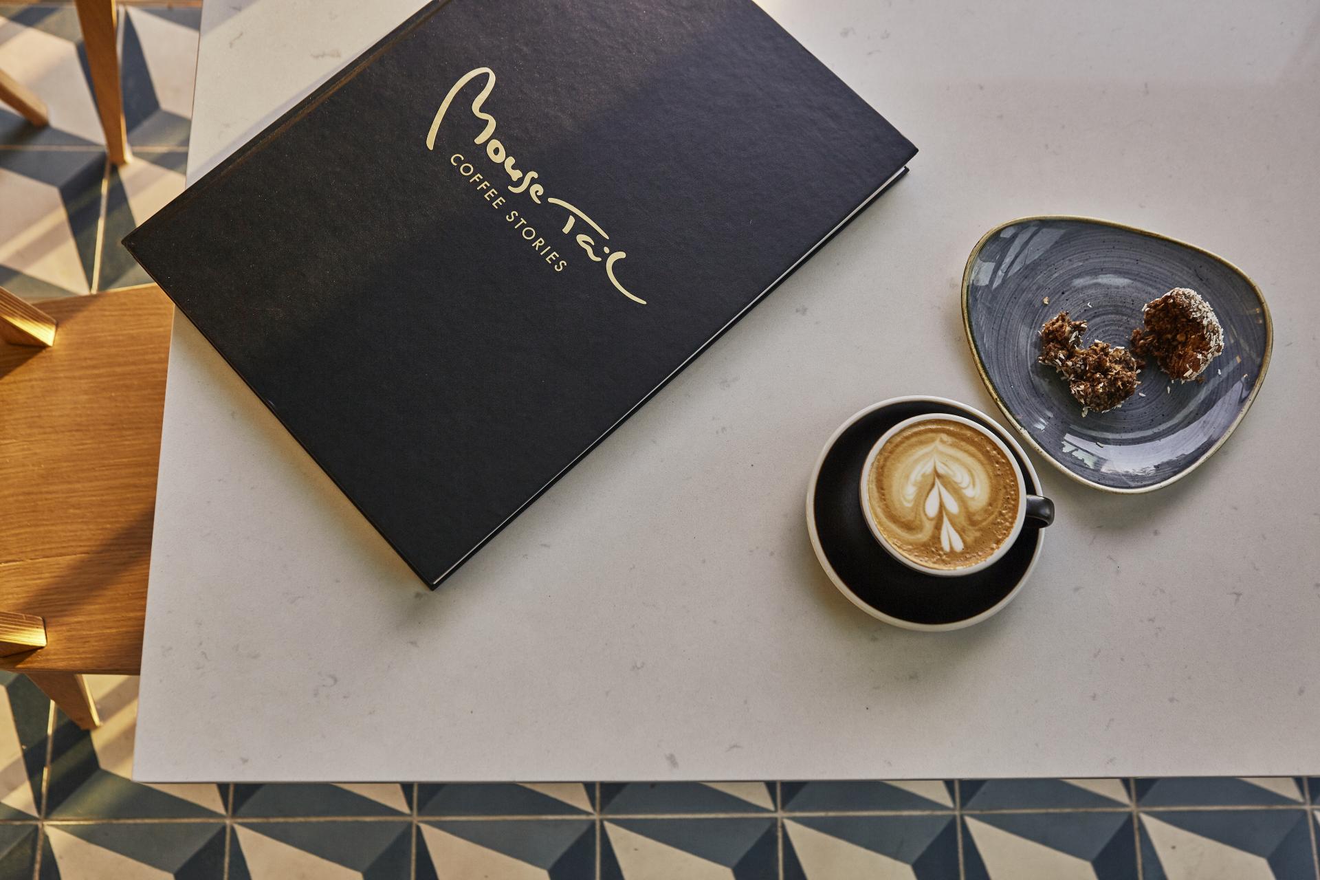 Mouse Tail Coffee Stories coffee on a quartz surface, accompanied by a dessert plate, showcasing a modern café setting.