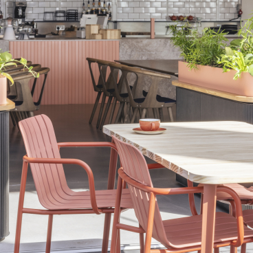 Modern café interior featuring vibrant coral chairs and lush greenery, highlighting popular design trends in hospitality for 2022.