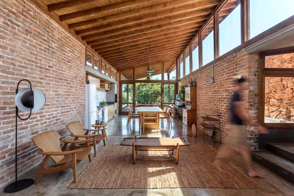Modern interior of The Lake House by Solo Arquitetos, featuring exposed brick walls and panoramic windows overlooking nature.