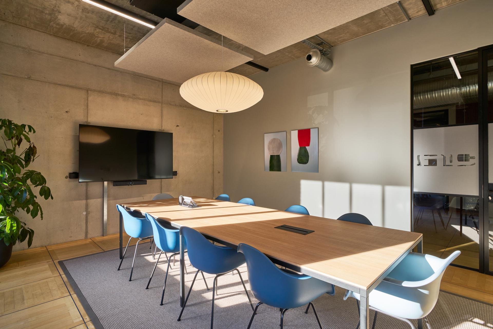 Modern conference room featuring a large wooden table, blue chairs, and vibrant wall art in a sustainable workspace.