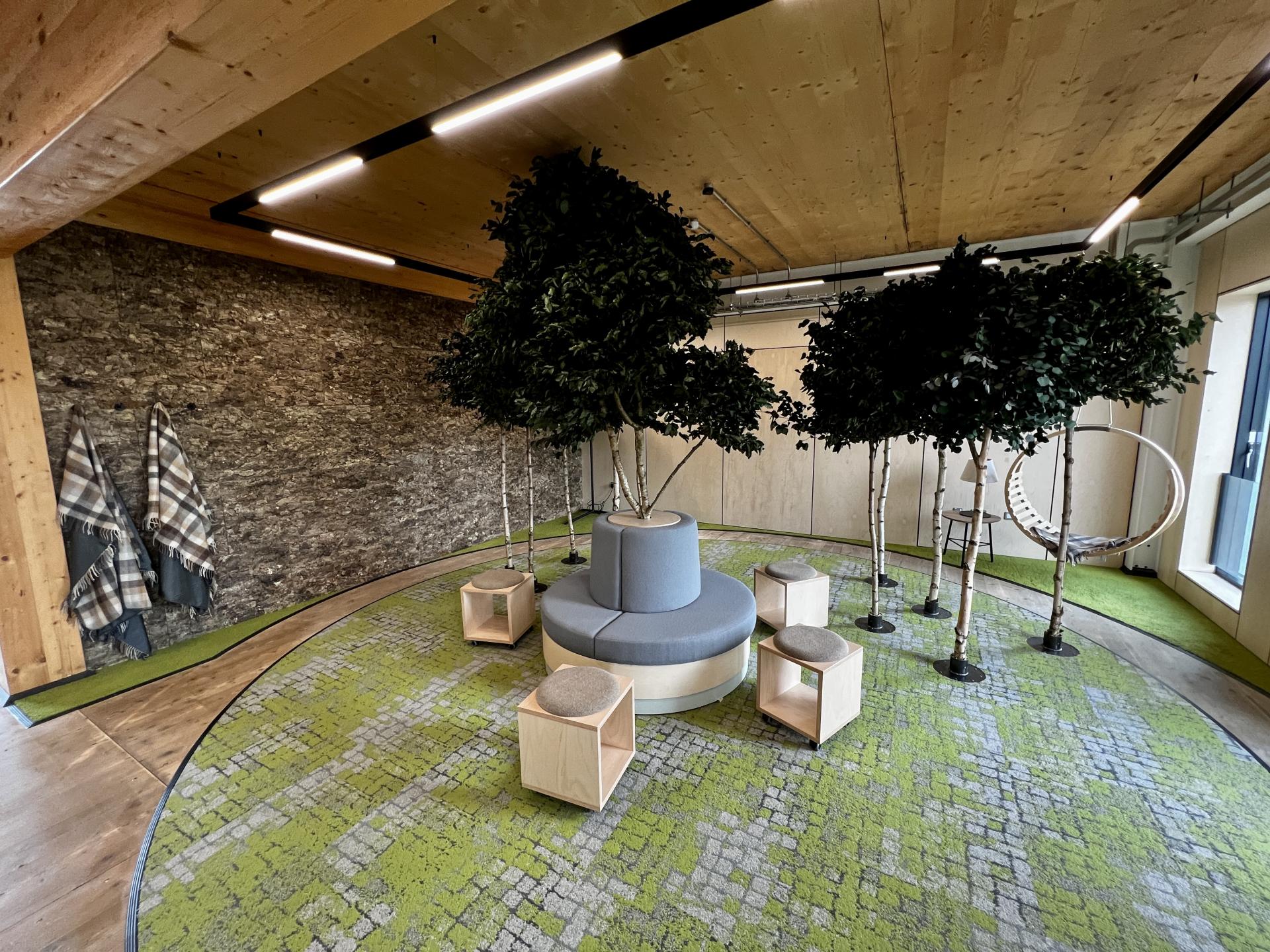 Innovative workspace featuring indoor trees, circular seating, and a green carpet, emphasizing Leeds' net zero carbon design.