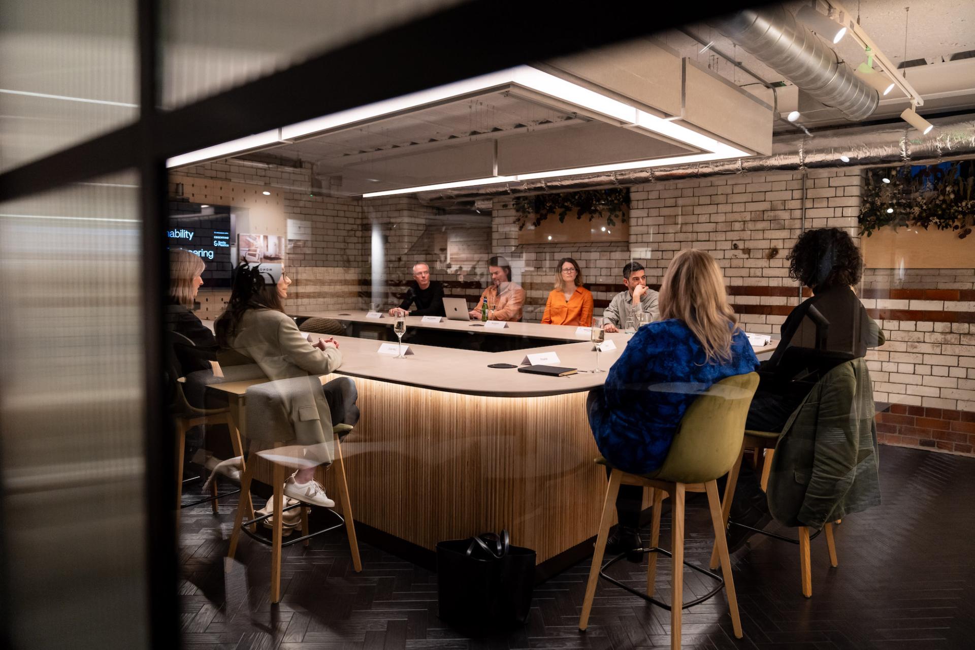 Participants engage in a roundtable discussion about sustainability and value engineering in a modern meeting room.