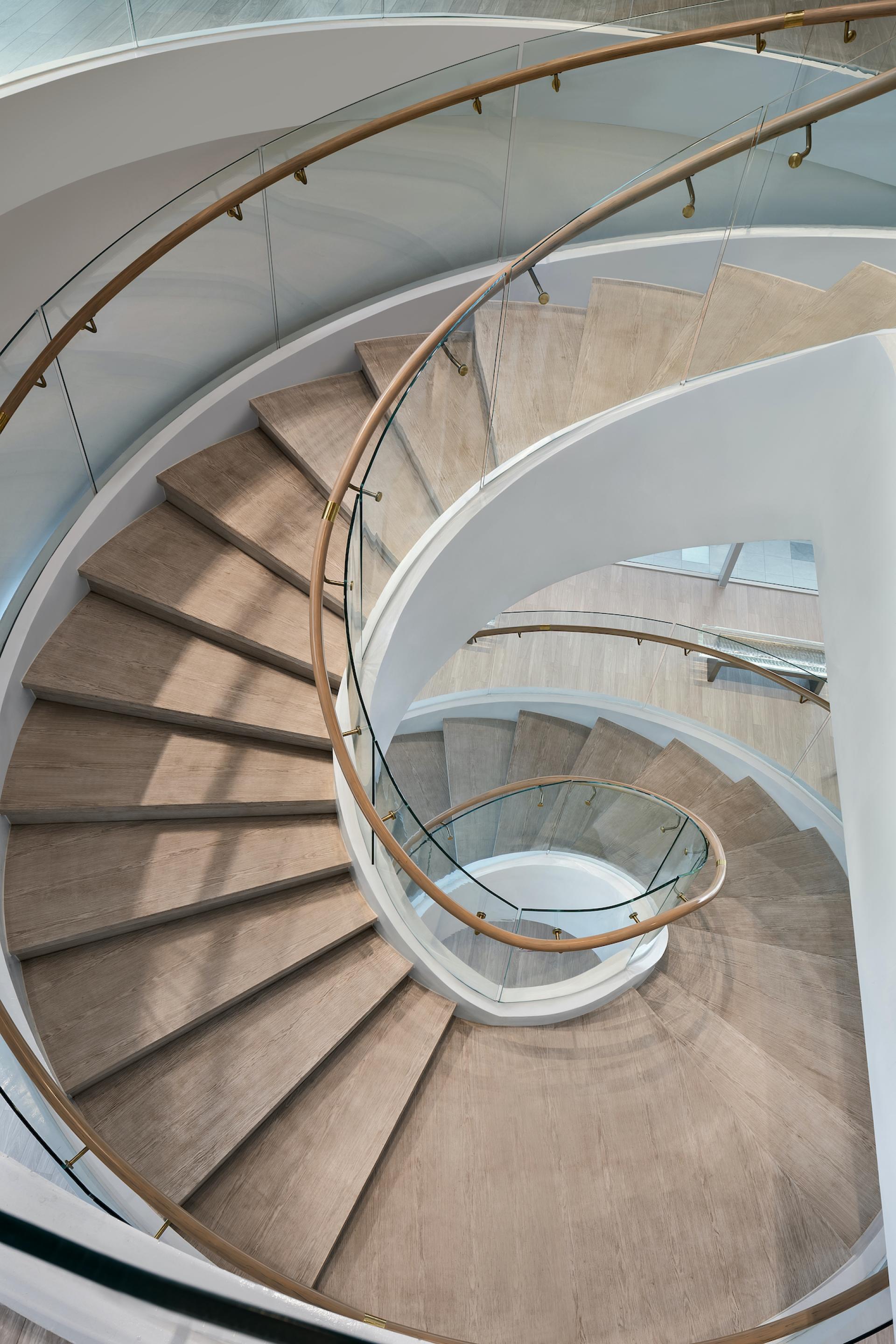 Stylishly designed spiral staircase featuring wooden steps, glass railing, and modern architectural elements for the Symbiotic Island bookshop.