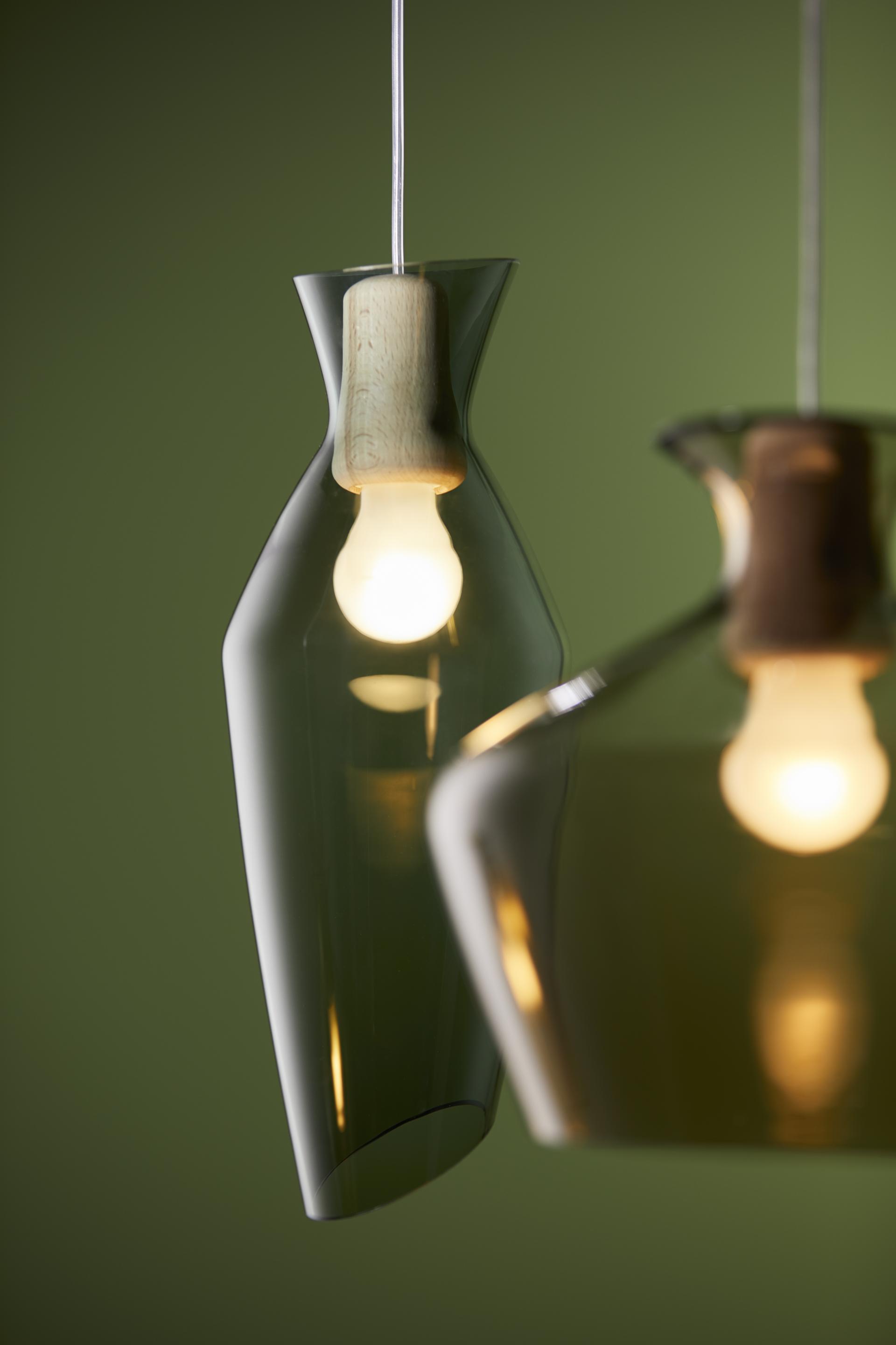 Elegant Malvasia lamp by Fabbian, featuring rounded shapes, wooden details, and warm glowing light against a green backdrop.