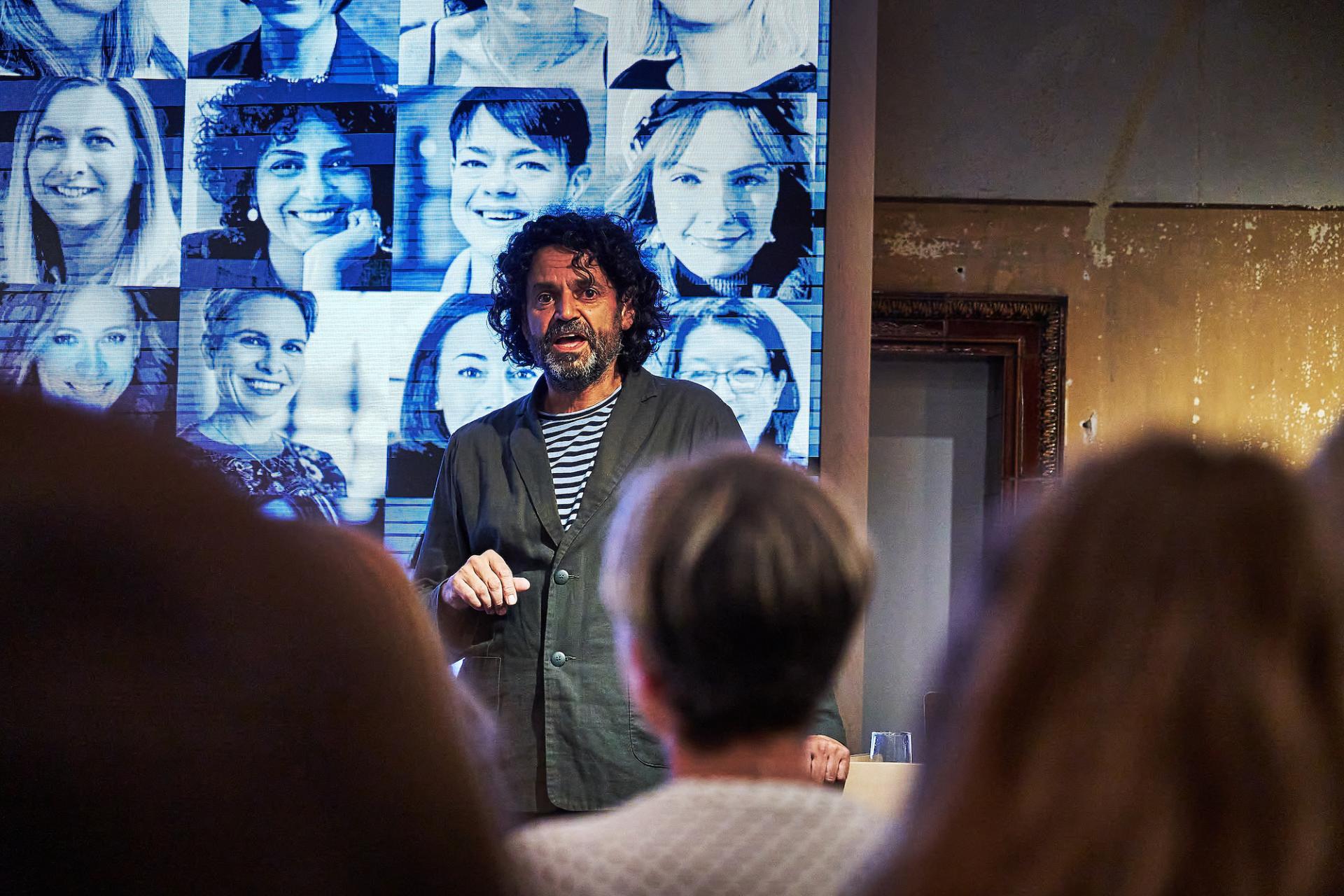 Speaker presents at the 42 Gathering event, featuring a backdrop of podcast guests' portraits celebrating 42 Roles in the Built Environment.