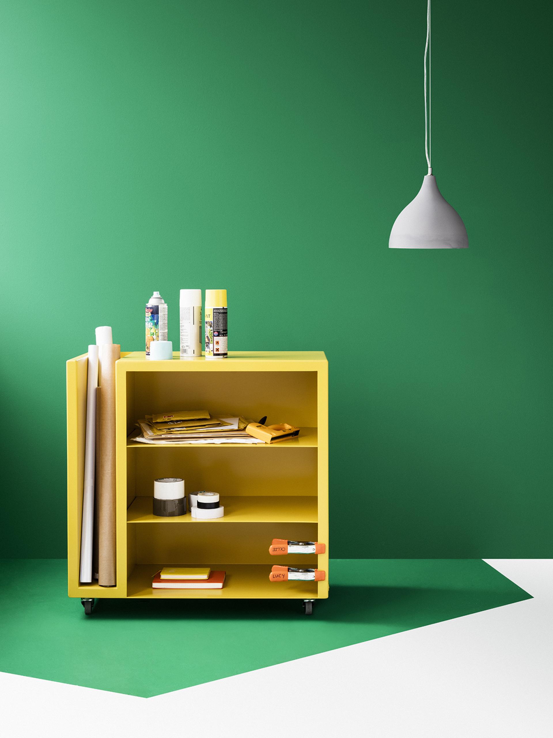 Bright yellow mobile storage unit filled with art supplies, against a vibrant green wall, showcasing functional furniture design.