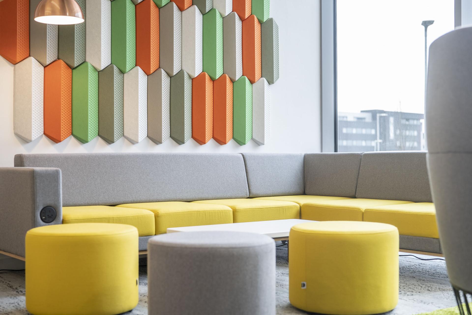 Brightly colored flexible furniture in an office space, featuring a gray and yellow couch with round seating and textured wall panels.