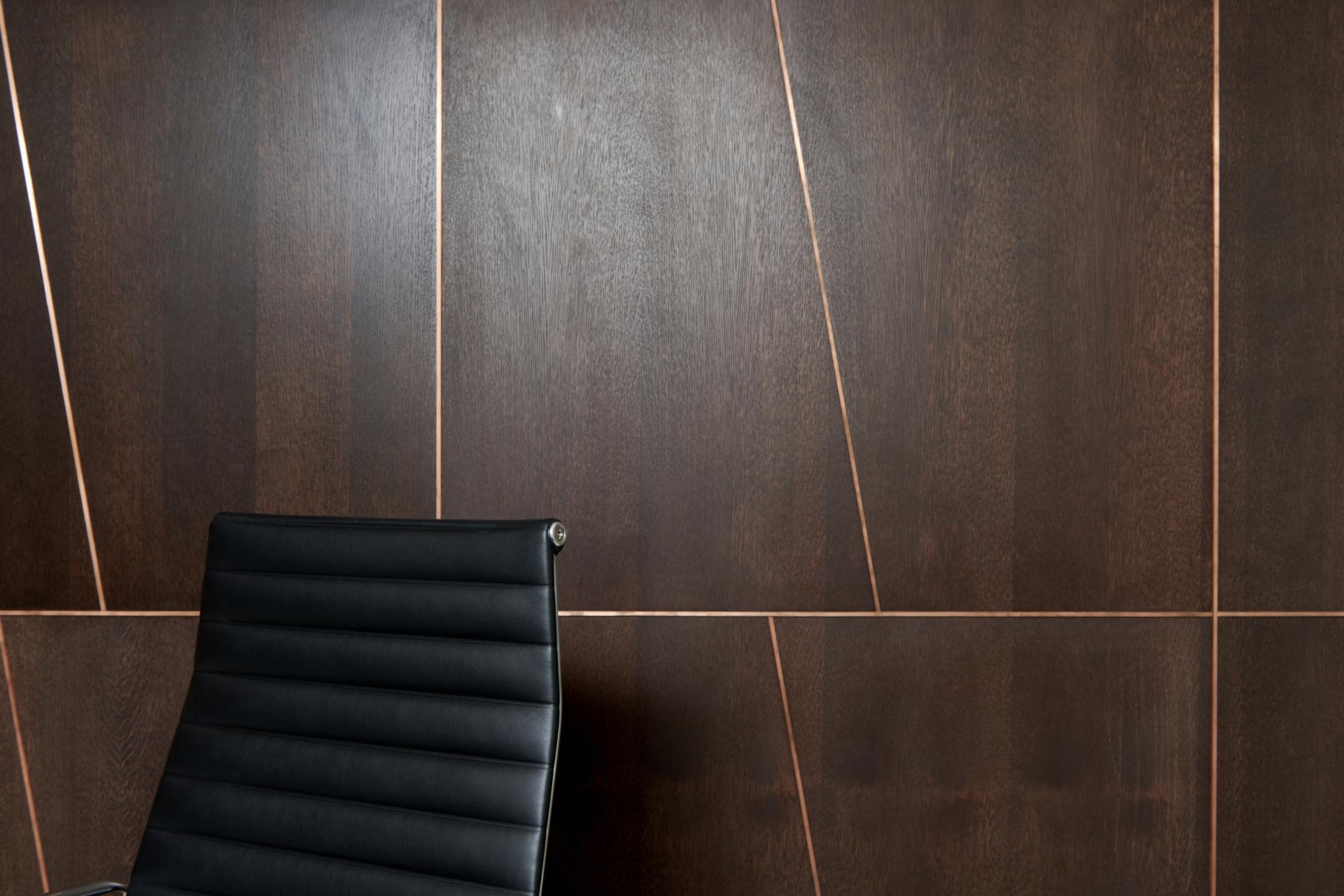 Elegant black chair against a dark wooden wall with copper accents, showcasing modern interior design at One Victoria Street.