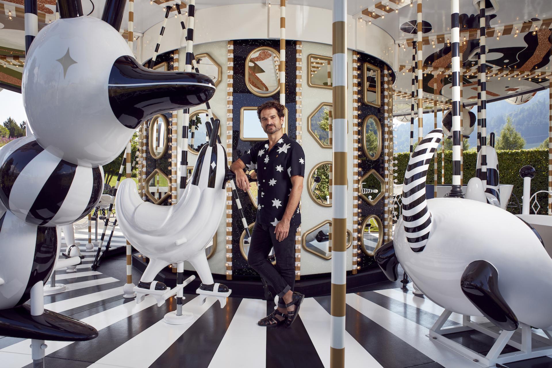 Jaime Hayon stands amid the playful, artistic carousel design featuring whimsical animal sculptures and vibrant patterns.