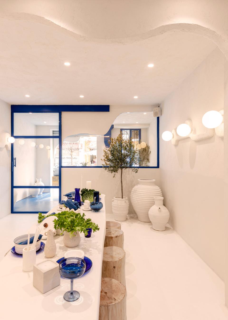 Modern Greek restaurant interior featuring a minimalist design, white decor, blue accents, and elegant table settings.