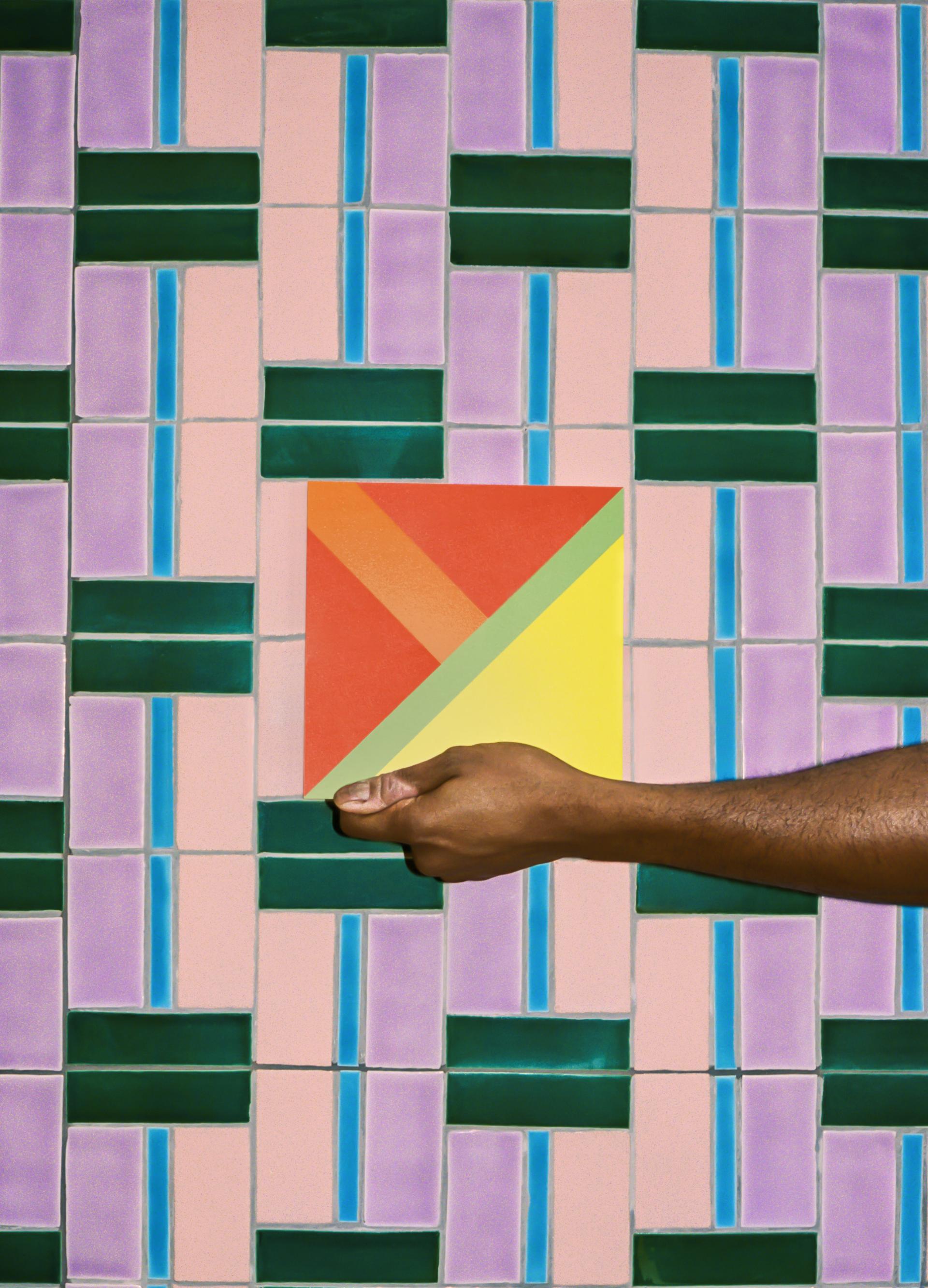 Colorful tiled wall featuring a hand holding a vibrant geometric tile, showcasing Domus and Yinka Ilori's collaboration at Clerkenwell Design Week.