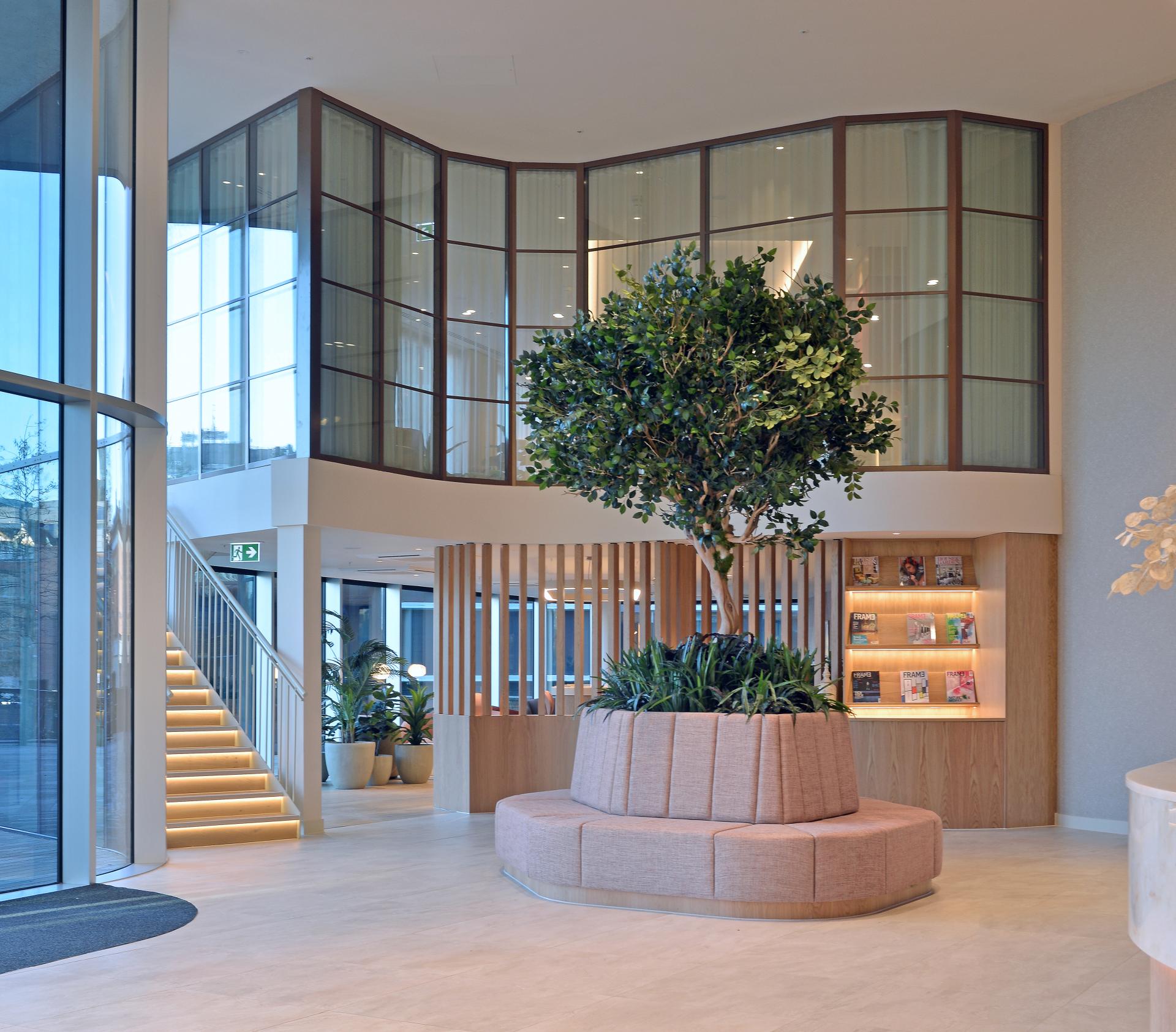 Modern architectural interior featuring a lush indoor tree, seating area, and natural light, highlighting smart workspace design.