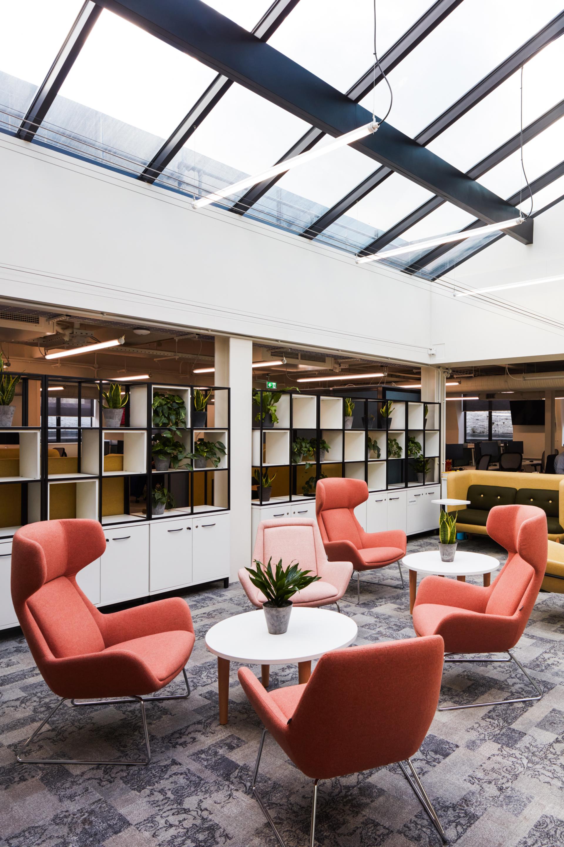 Modern office space featuring stylish seating, natural plants, and a skylight, promoting collaboration and innovation at Queen Mary University.
