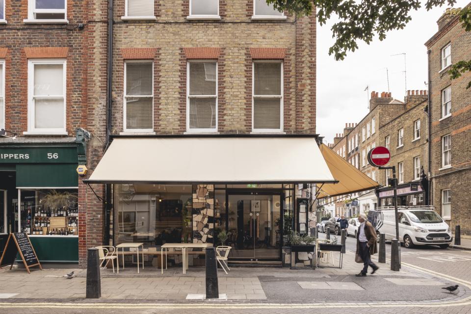 Exterior view of Honey & Co Bloomsbury, showcasing its inviting entrance, outdoor seating, and distinctive architectural design.
