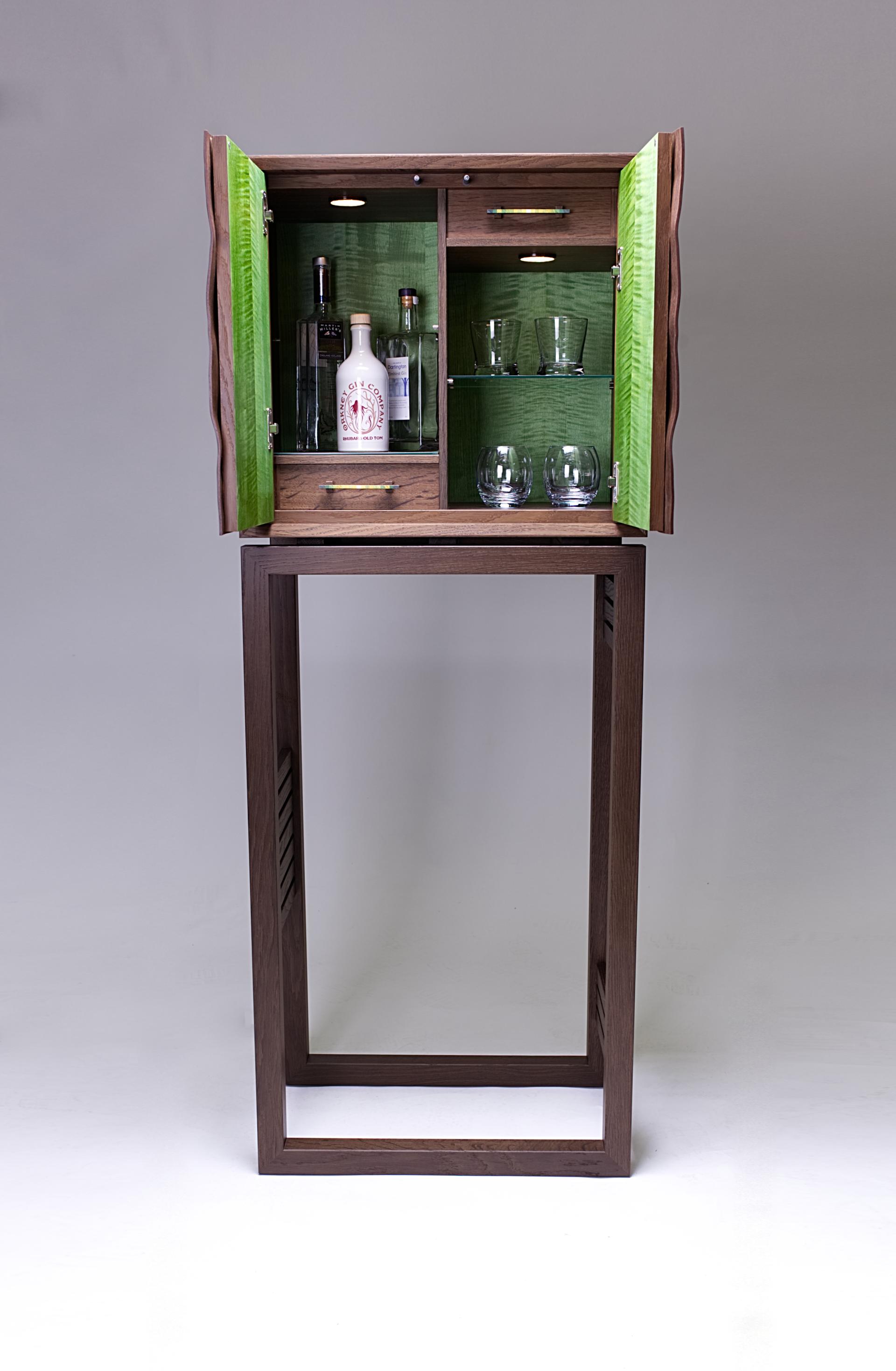 Stylish wooden cabinet with green interior, showcasing glassware and bottles, crafted by artist Kevin Stamper.
