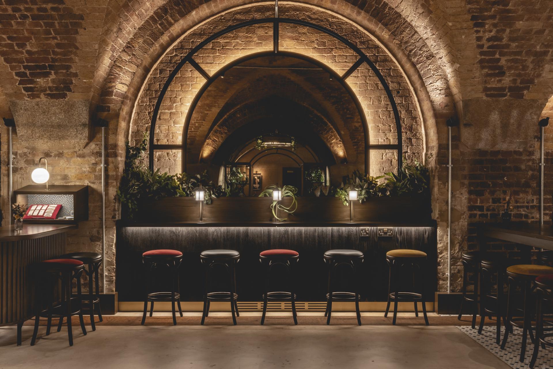 Stylish interior of The Libertine, a new hospitality venue in London's historic Royal Exchange, featuring arched brickwork and bar seating.