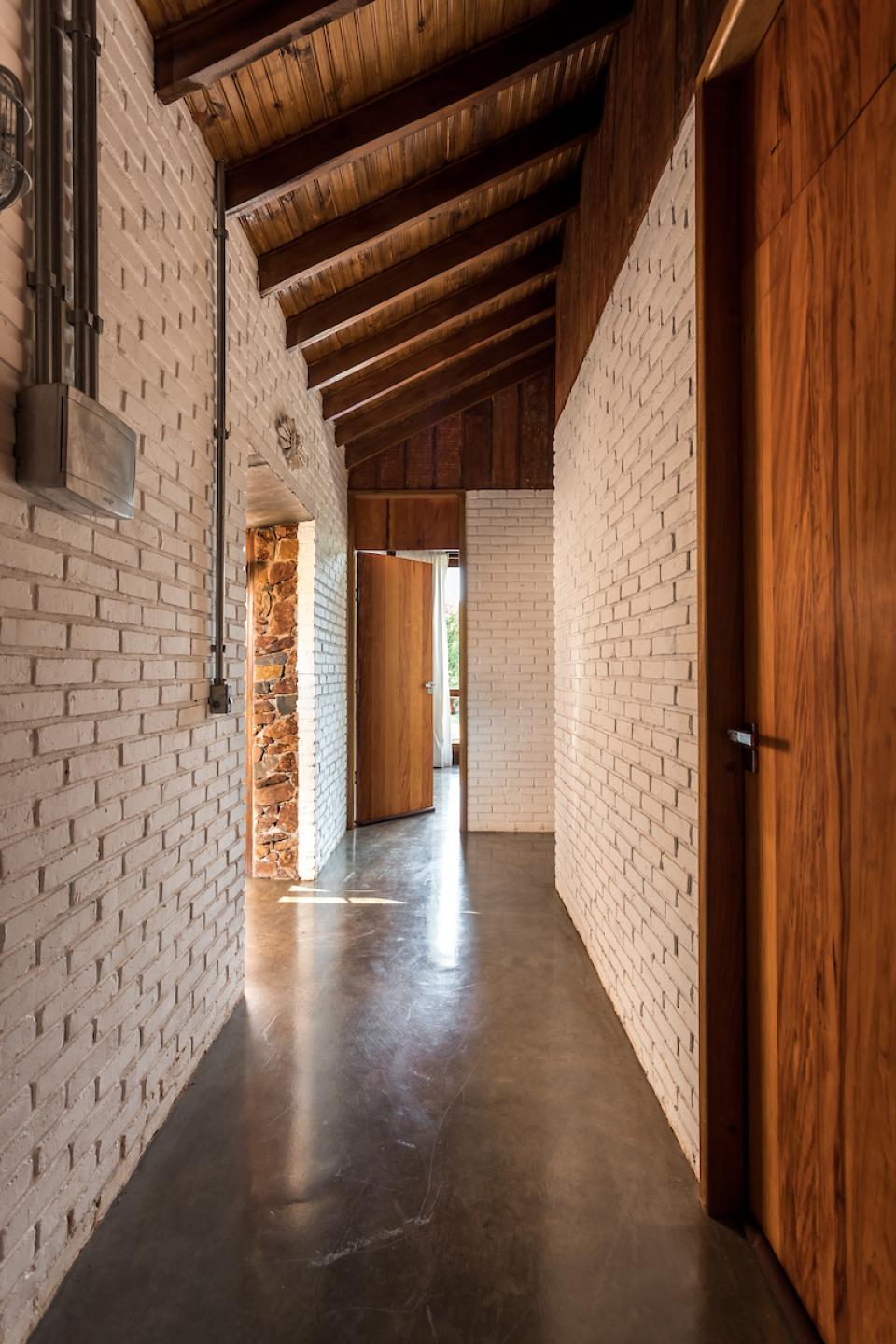 Modern hallway of The Lake House in Brazil, featuring white brick walls and wooden accents, showcasing architectural harmony with nature.