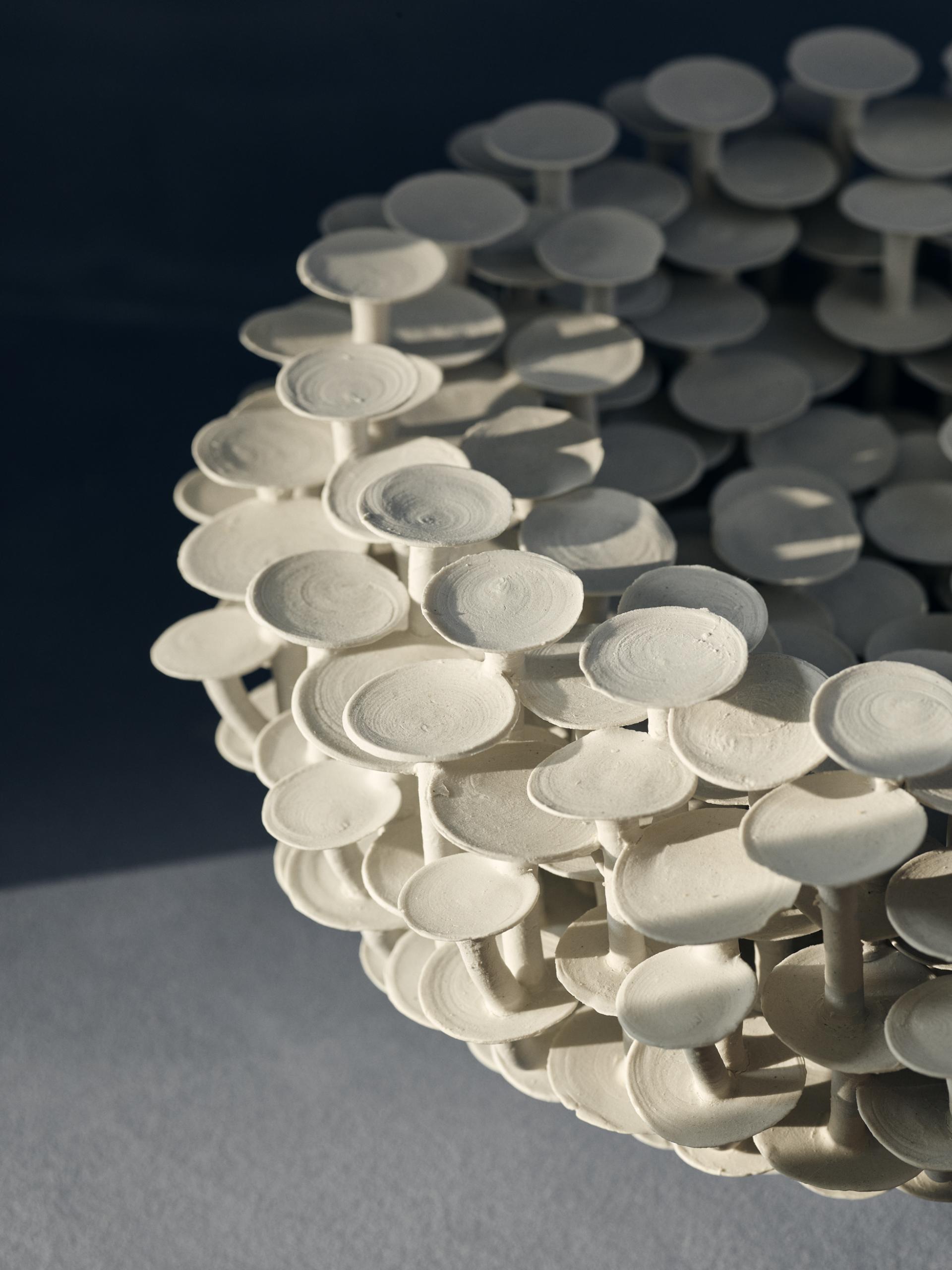 Sculptural ceramic artwork featuring numerous white, round shapes stacked in an intricate formation, showcasing contemporary craft artistry.