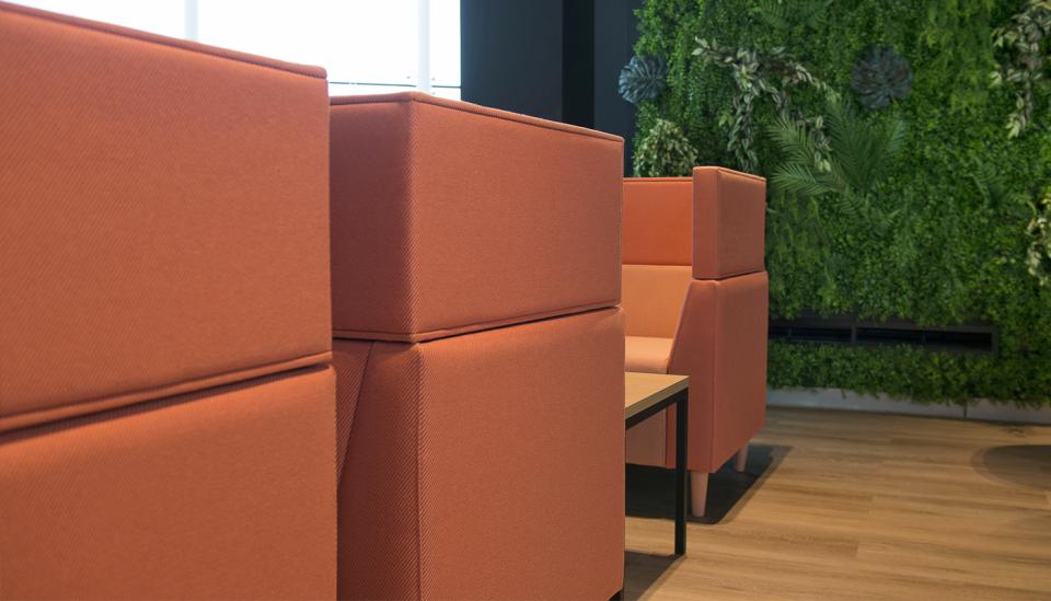 Vibrant orange seating contrasts with lush greenery in a modern workspace at Alderley Park, Cheshire.