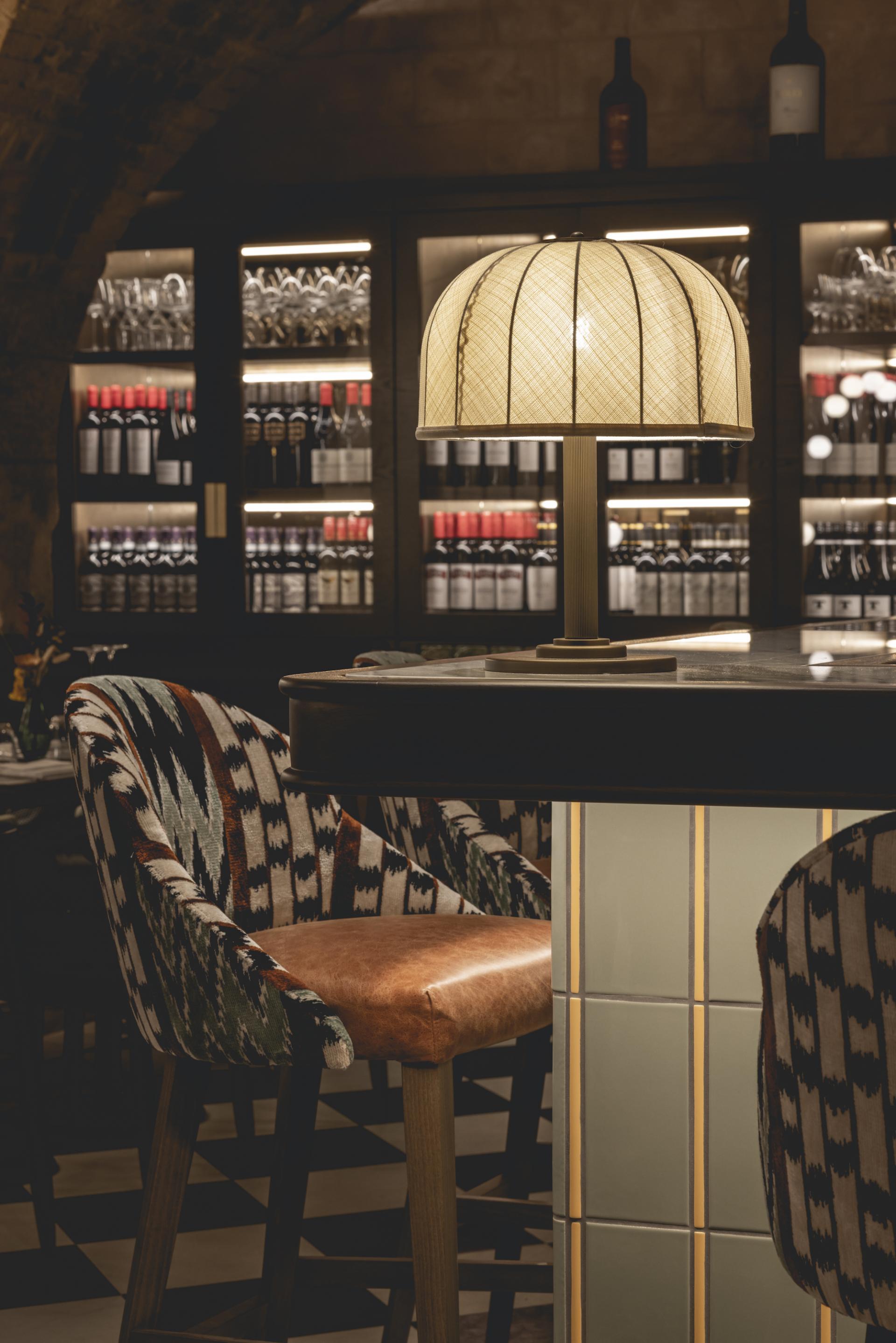 Elegant interior of The Libertine, featuring patterned chairs, a stylish lamp, and a wine display in the background.