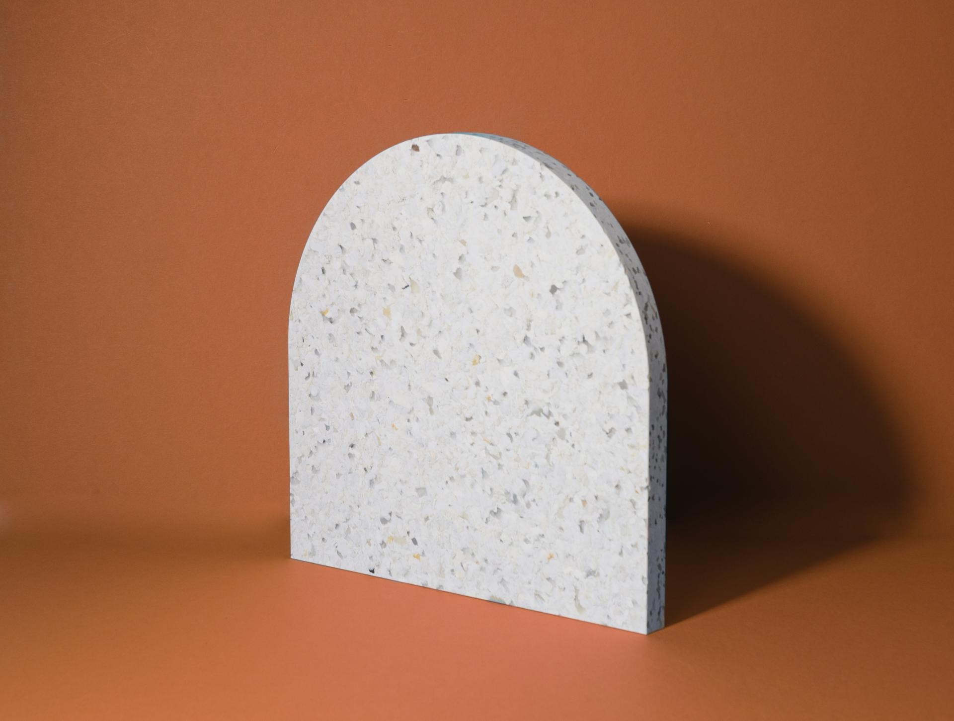 Textured white surface in an arch shape against a warm brown background, showcasing contemporary design trends at Surface Design Show 2023.