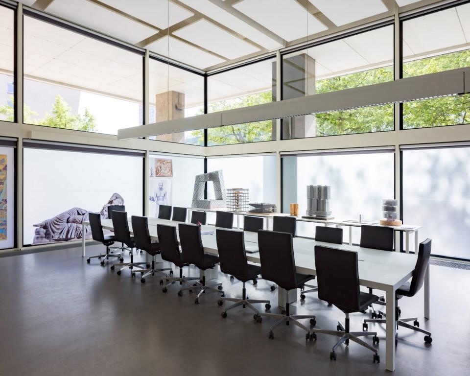 Modern architect studio featuring a sleek meeting table, ergonomic chairs, and large windows with natural light.