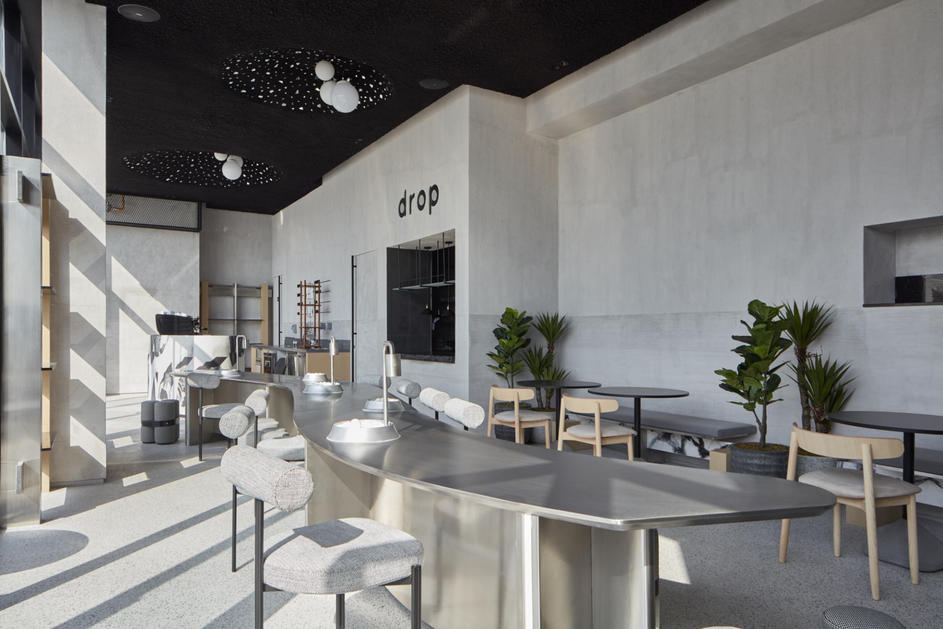 Minimalist interior of Drop Coffee's Abu Dhabi outpost featuring sleek surfaces, plants, and modern seating arrangements.