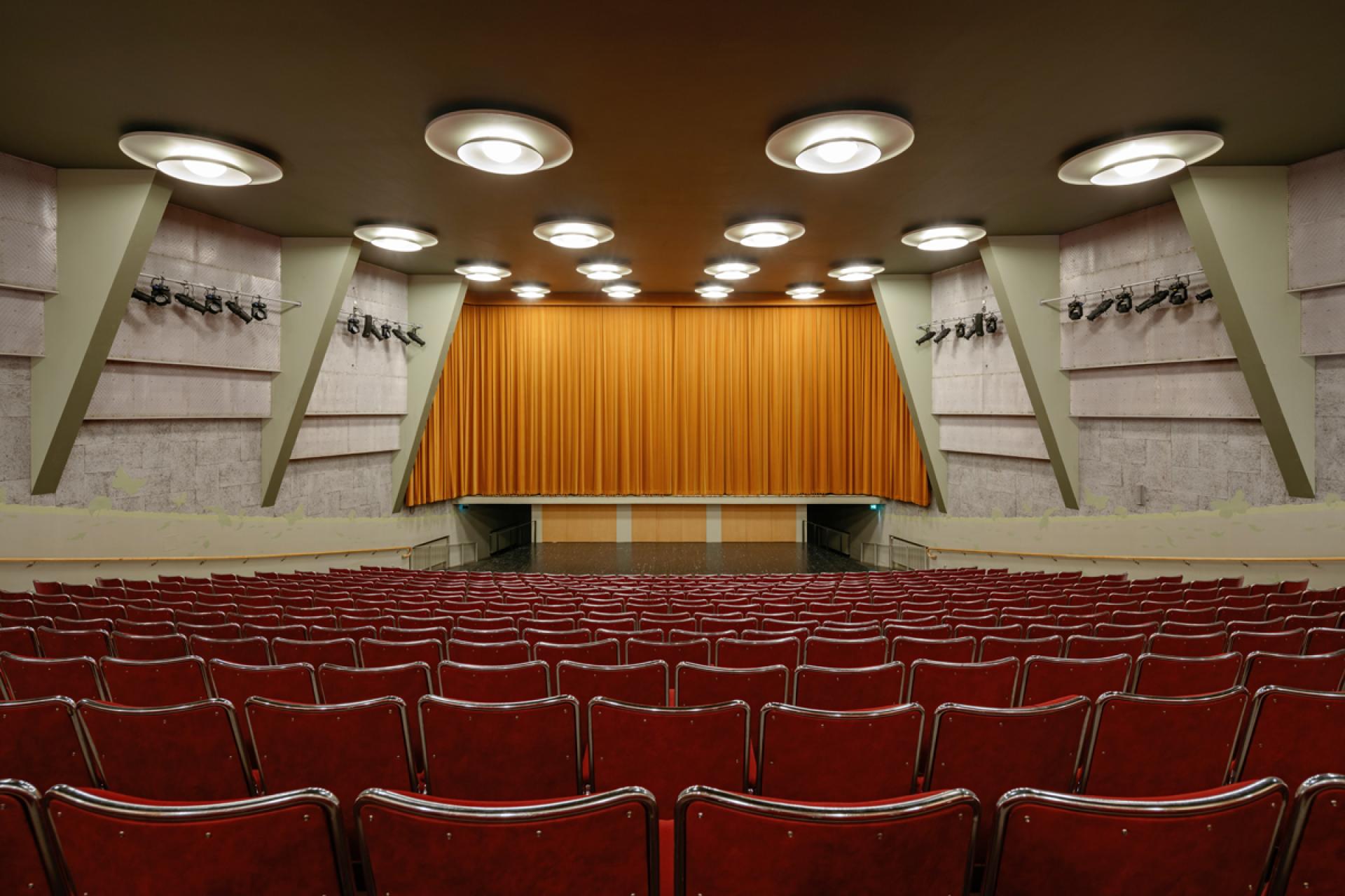 Modern auditorium with red chairs and an orange curtain, part of Helsinki's new art museum designed by JKMM Architects.
