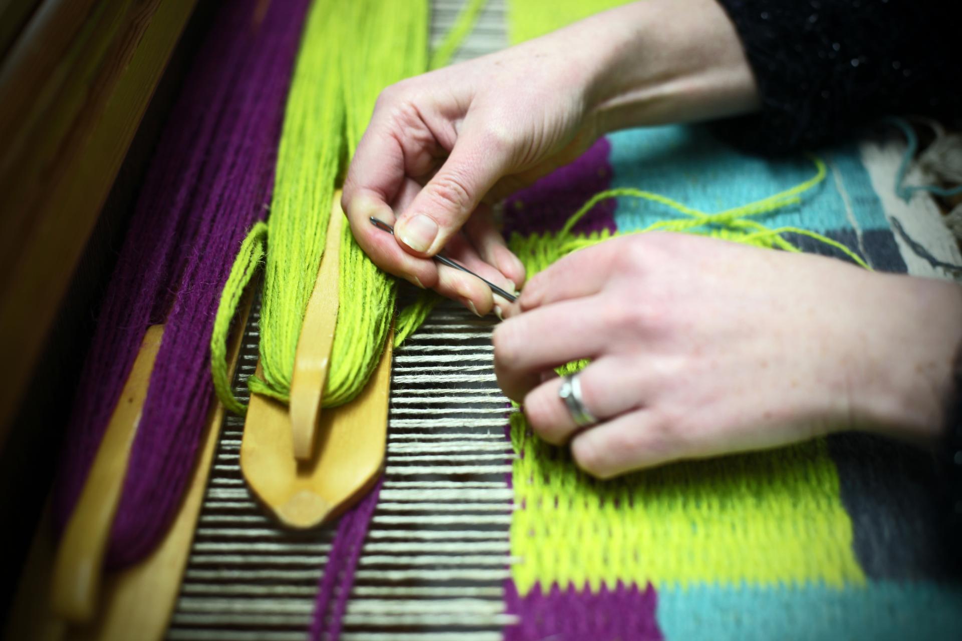 Hands skillfully weaving vibrant threads on a loom, showcasing intricate details of Scandinavian textile design techniques.