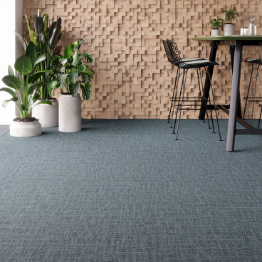Contemporary workplace featuring Forbo's Tessera Accord flooring, indoor plants, and stylish bar seating against a textured wood wall.