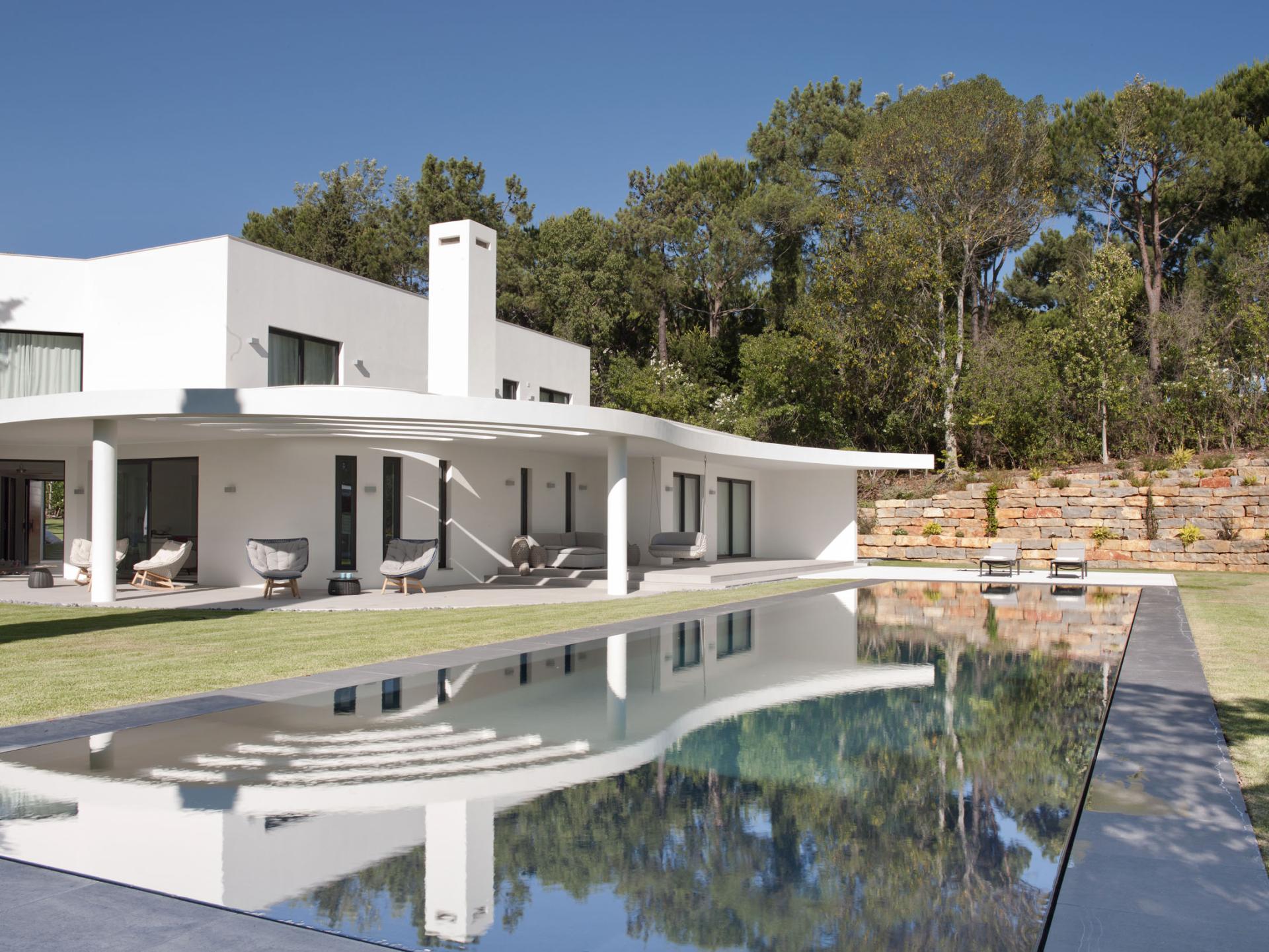 Contemporary white villa with a sleek design, reflecting in a serene swimming pool amidst lush Portuguese greenery.