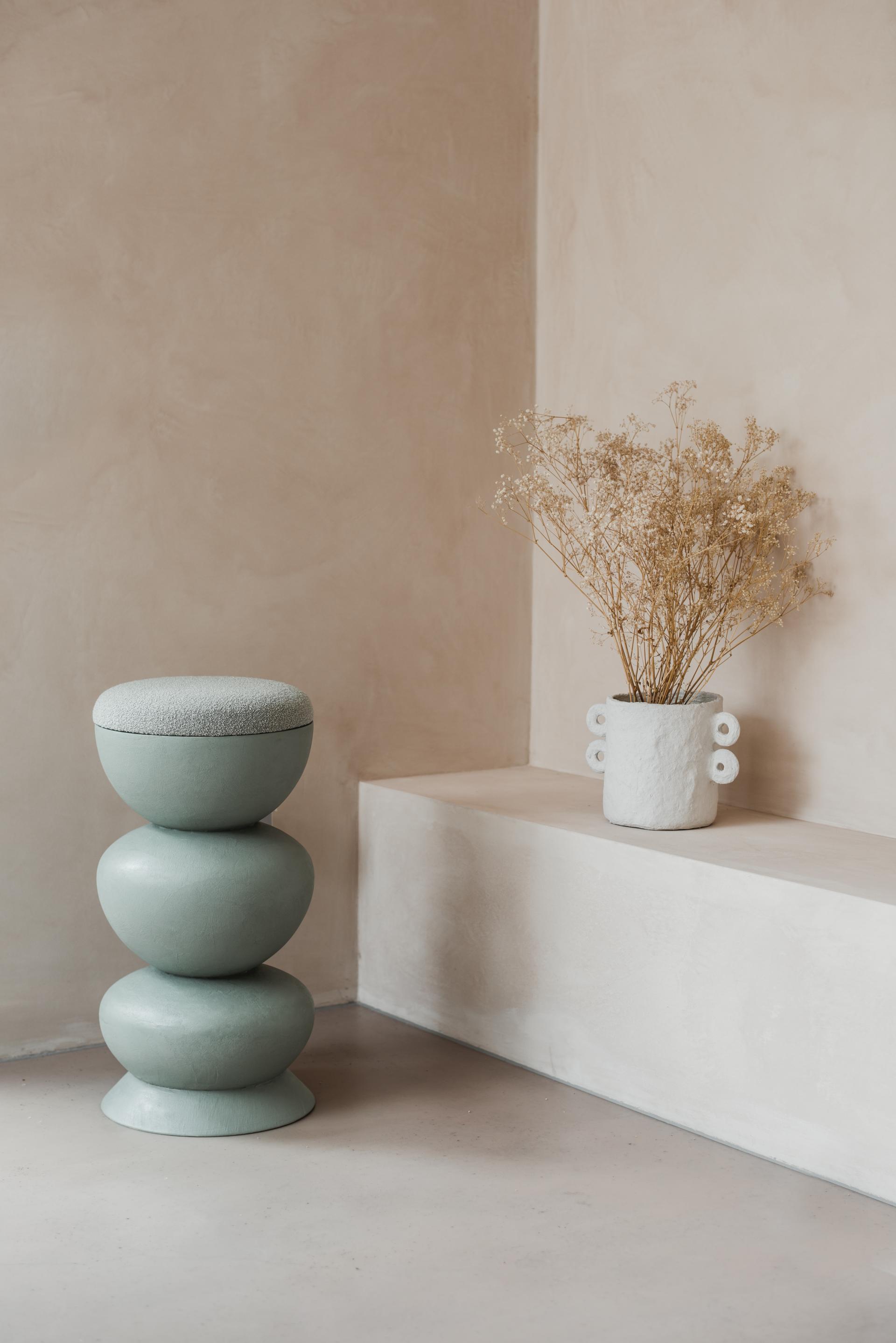 Curvaceous green stool and decorative white vase with dried flowers, reflecting Sella Concept's artistic furniture design inspired by Hampstead Ladies’ Pond.