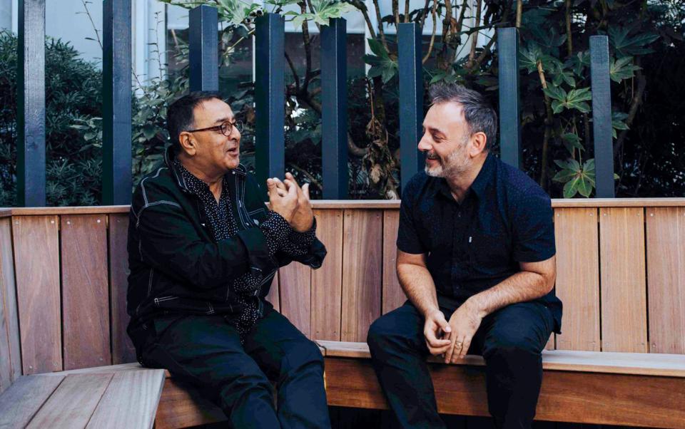 Jon Humphreys and Atul Bansal engaging in conversation on a wooden bench surrounded by greenery, reflecting community and creativity.
