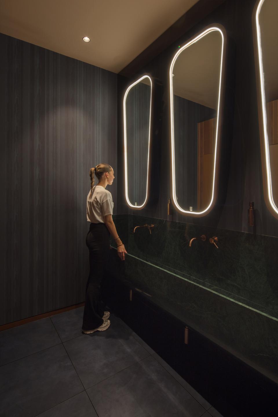Chic restroom interior featuring glowing mirrors, a green marble sink, and a stylish visitor at M'Arks Sky Bar, London.