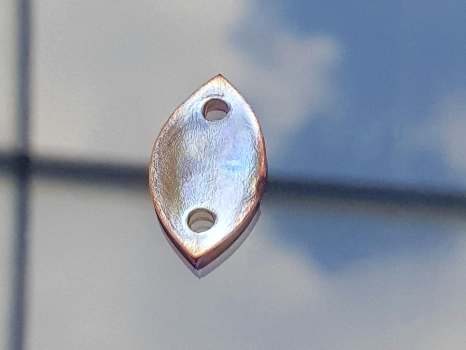 Iridescent bio sequins made from wood, showcasing a shimmering surface and two attachment holes for sustainable design.