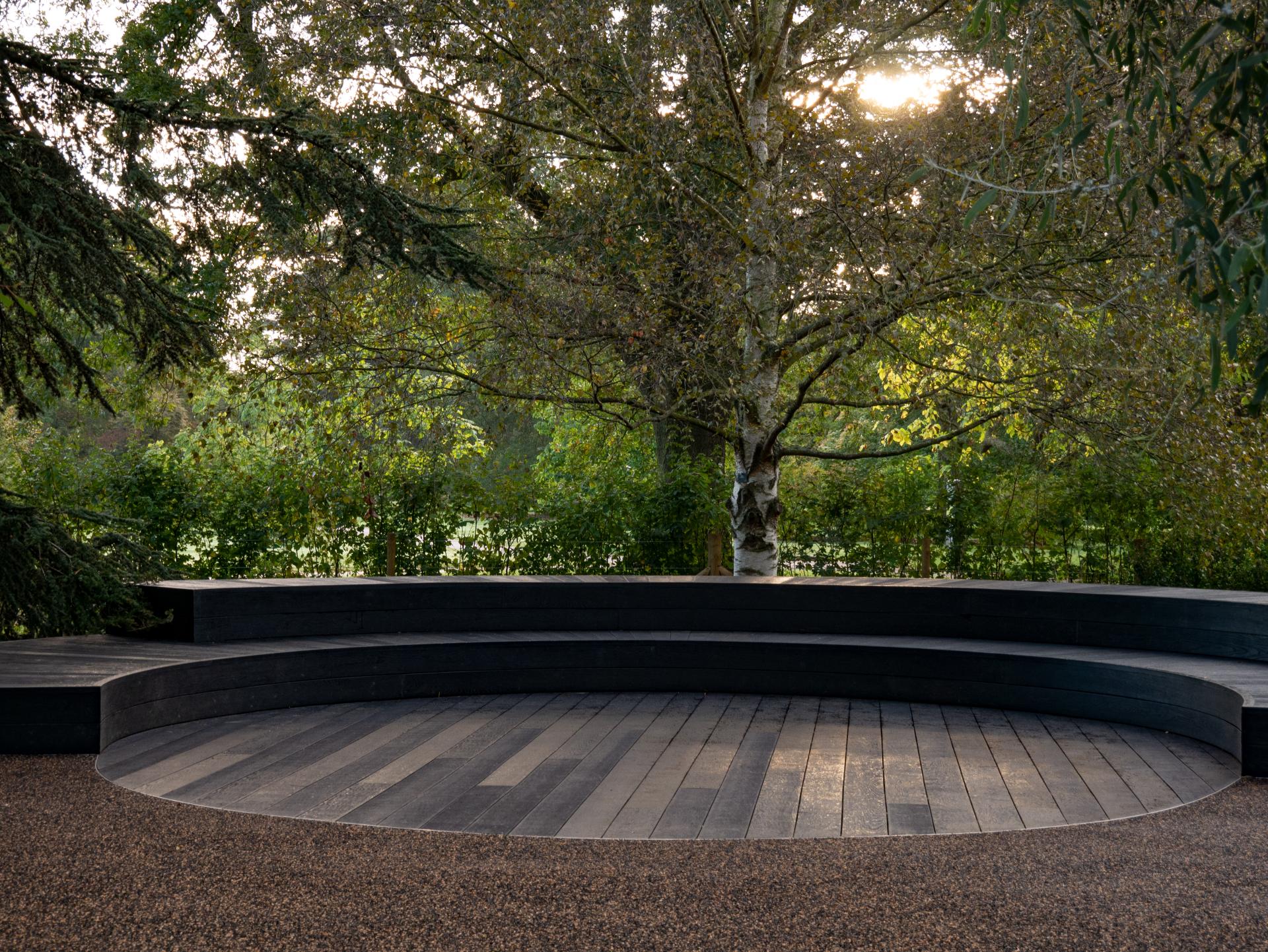 Curved black wooden seating area surrounded by vibrant greenery at the Royal Botanic Gardens, Kew, blending heritage and modern design.