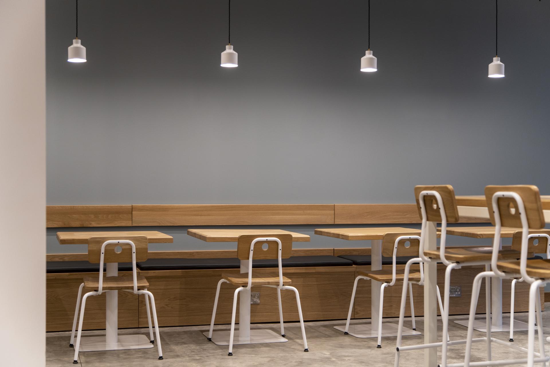 Minimalist interior of Bread Lab Bakery featuring wooden benches, simple tables, and pendant lighting against a muted wall.