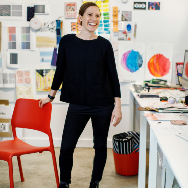 Designer Kelly Harris Smith stands in a vibrant workspace, showcasing her creative process for HBF Textiles' sustainable designs.