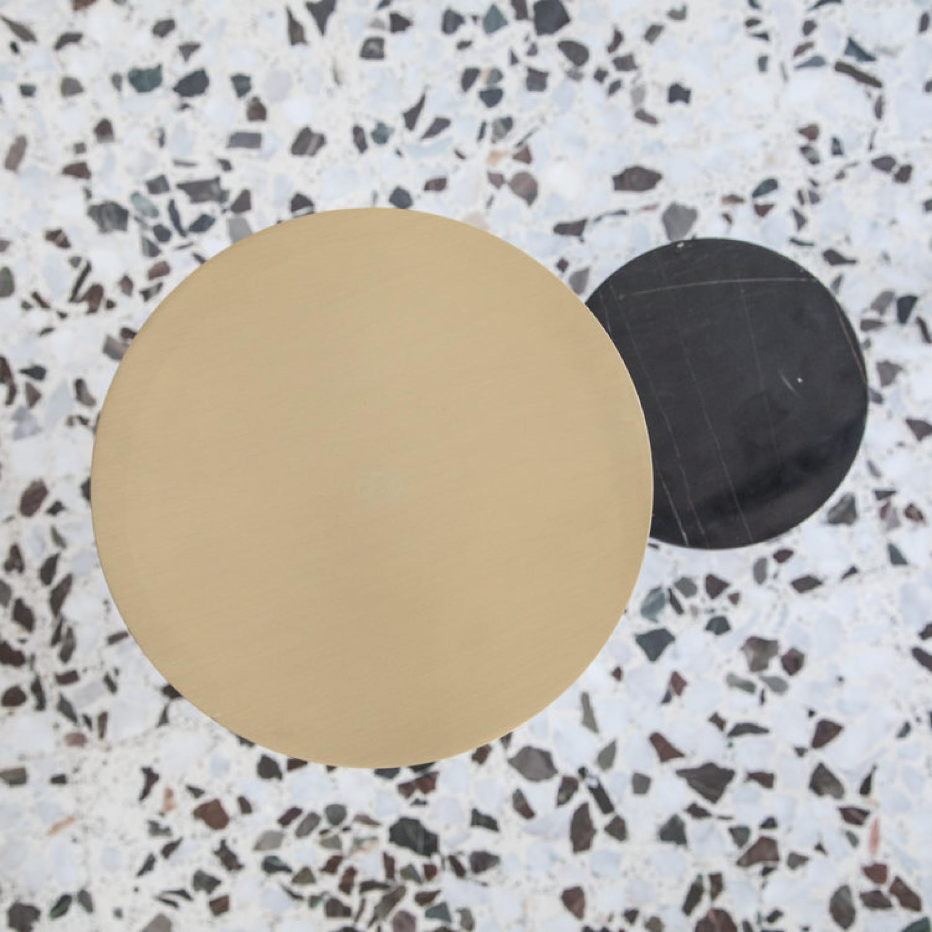 Geometric coffee table with gold and black circular surfaces on a speckled terrazzo floor, showcasing modern design.