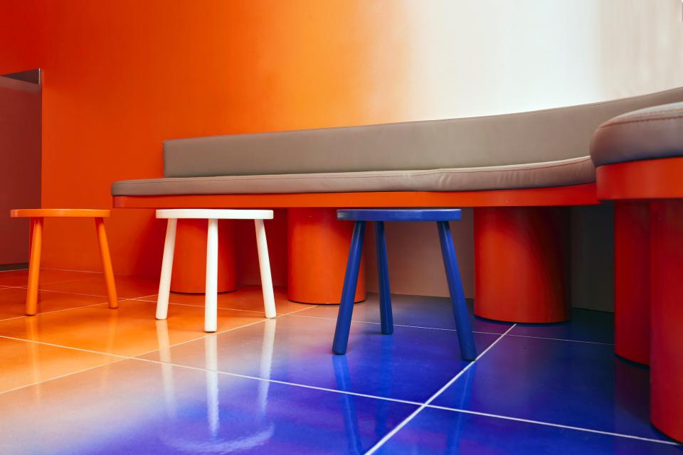 Vibrant interior of Café Nuances featuring colorful stools and an orange wall design, showcasing psychedelic decor by Studio Uchronia.