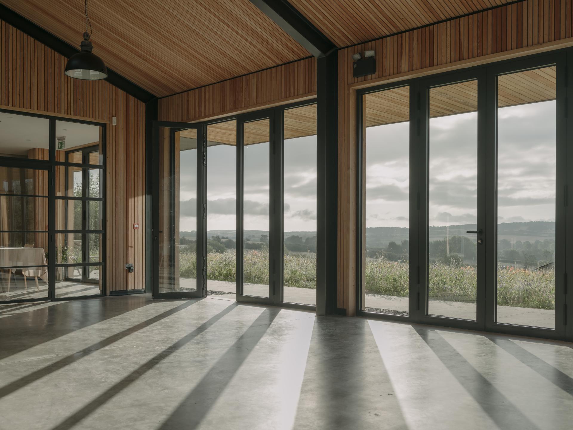 Interior of a sustainable farming education centre with large windows, showcasing natural light and scenic views of the Cotswolds.