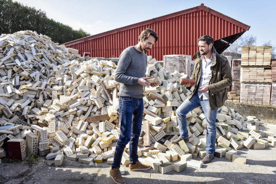 Co-founders of StoneCycling discuss sustainable brick production amid a large pile of recycled materials.