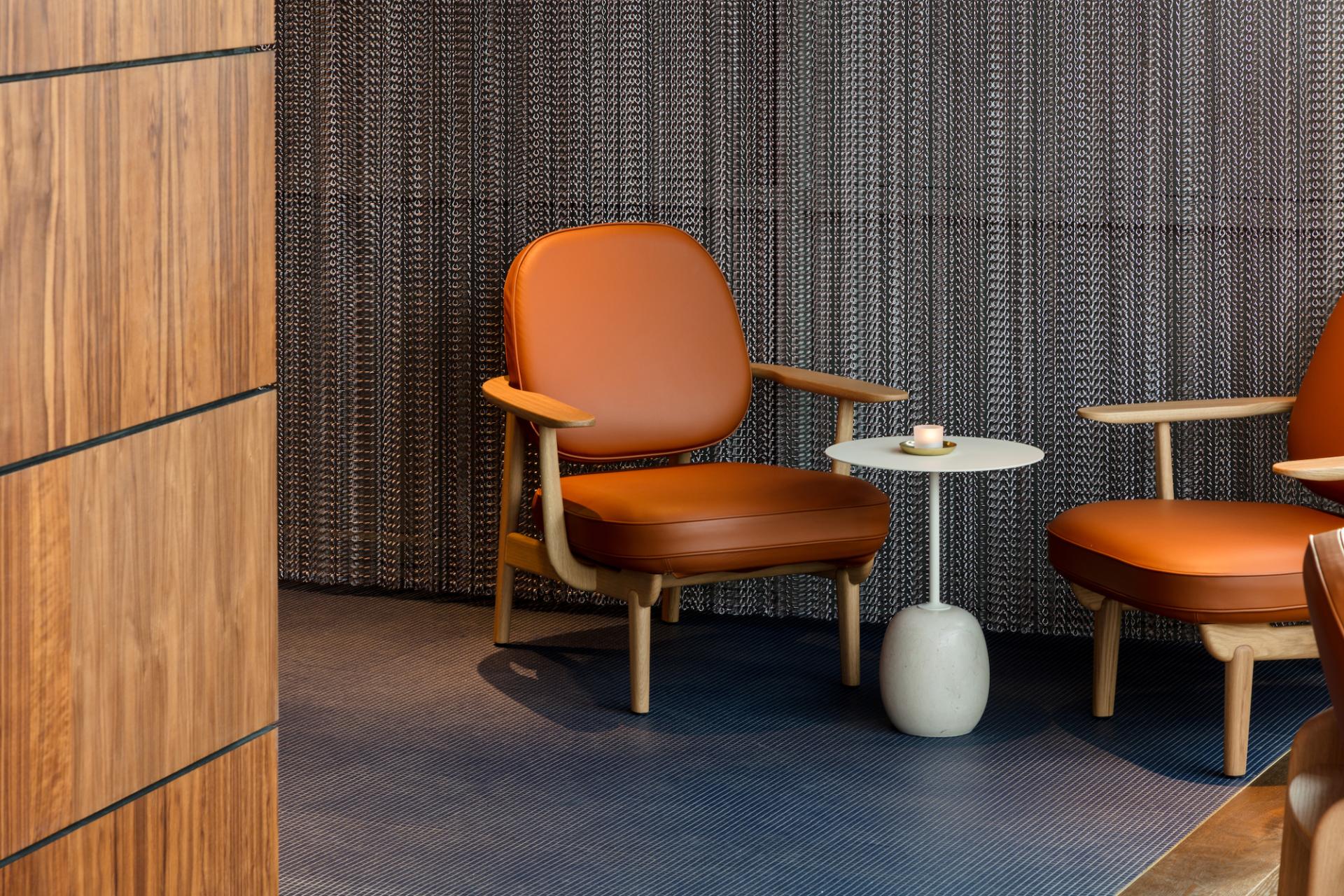 Stylish orange leather chairs beside a minimalist side table, set against a textured backdrop in M'Arks Sky Bar, London.