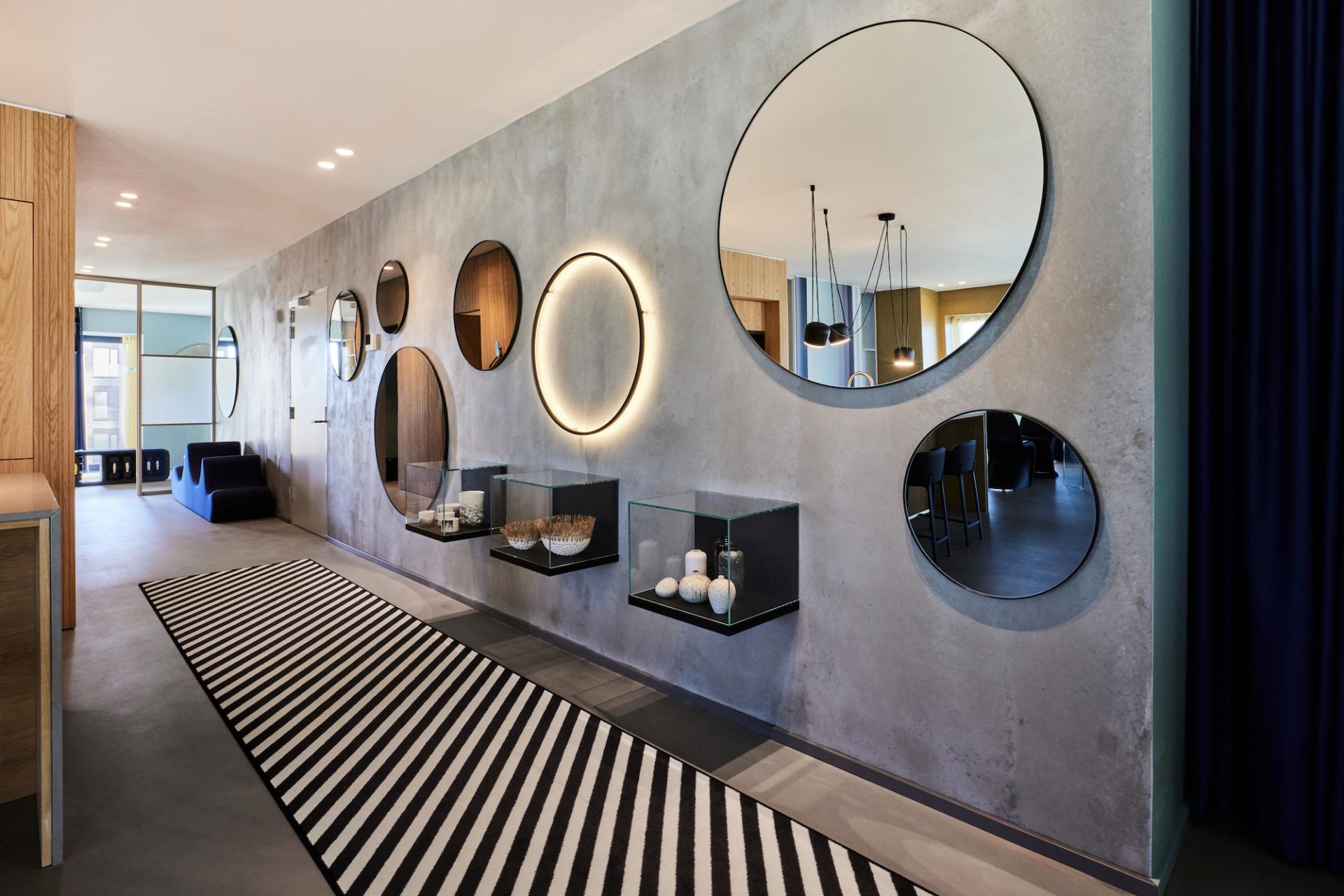 Modern interior hallway featuring circular mirrors, a black and white striped rug, and elegant decorative displays.